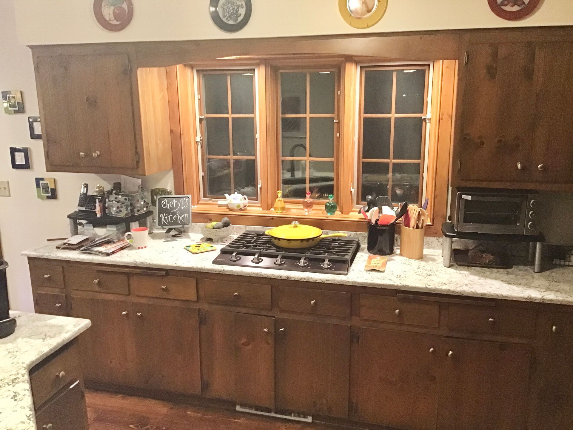 Wooden kitchen with granite counters, central window, and a stove with a yellow pan on top.