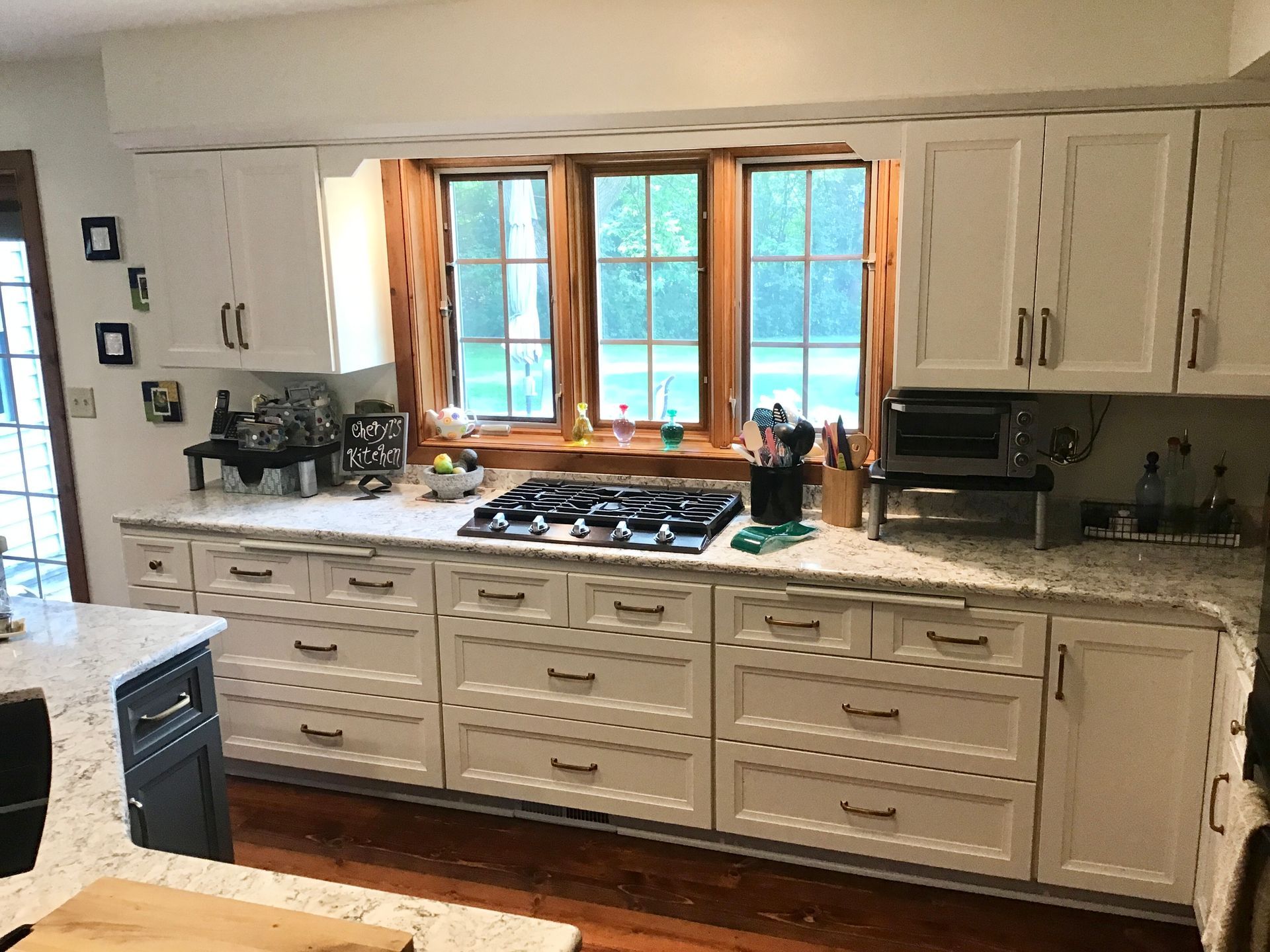 Bright kitchen with cream cabinets, marble countertops, and a large window above the stove.
