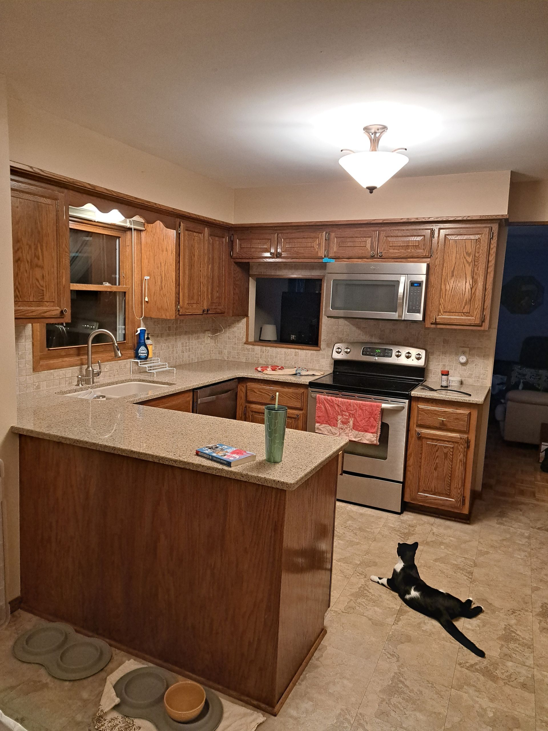 Warm kitchen with wooden cabinets, granite island, and a black cat lying on the floor.