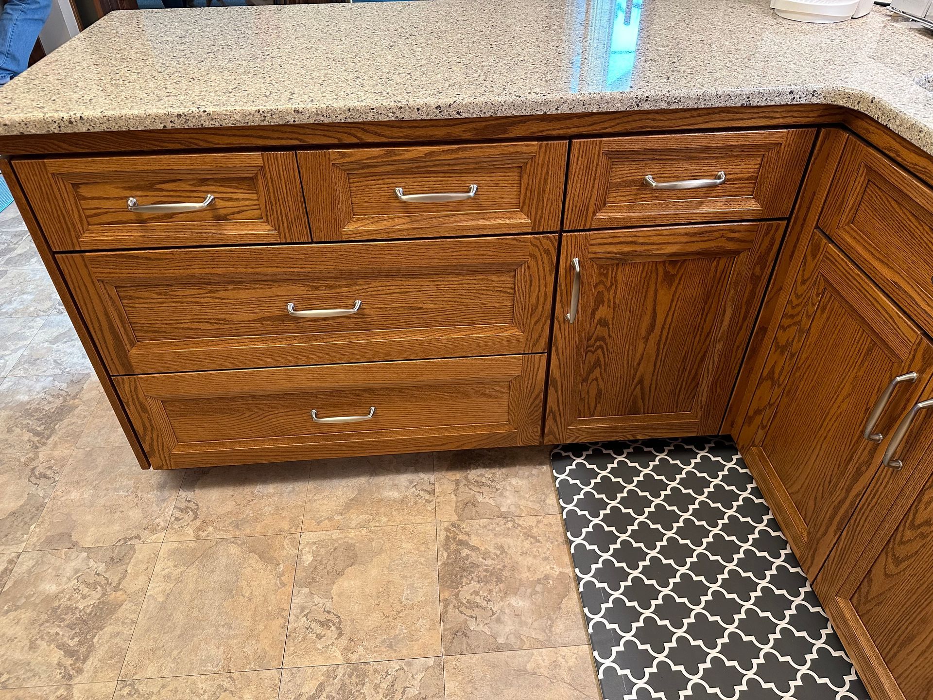 Woodgrain kitchen cabinets with granite countertop and patterned tile floor corner.