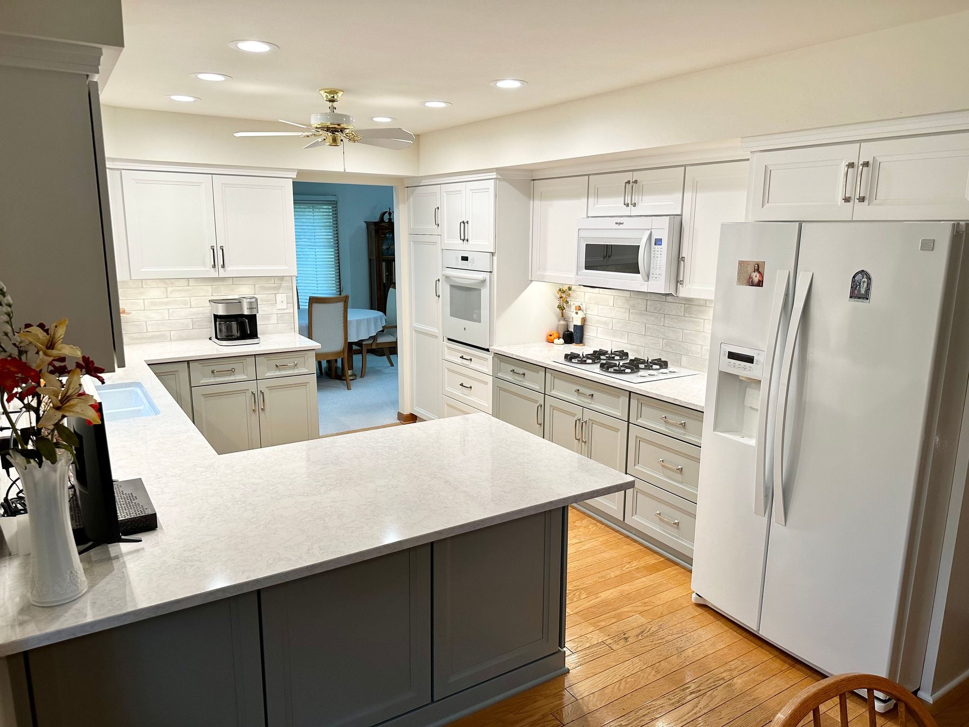 Bright white kitchen with island, gray cabinets, white appliances, and wood floors