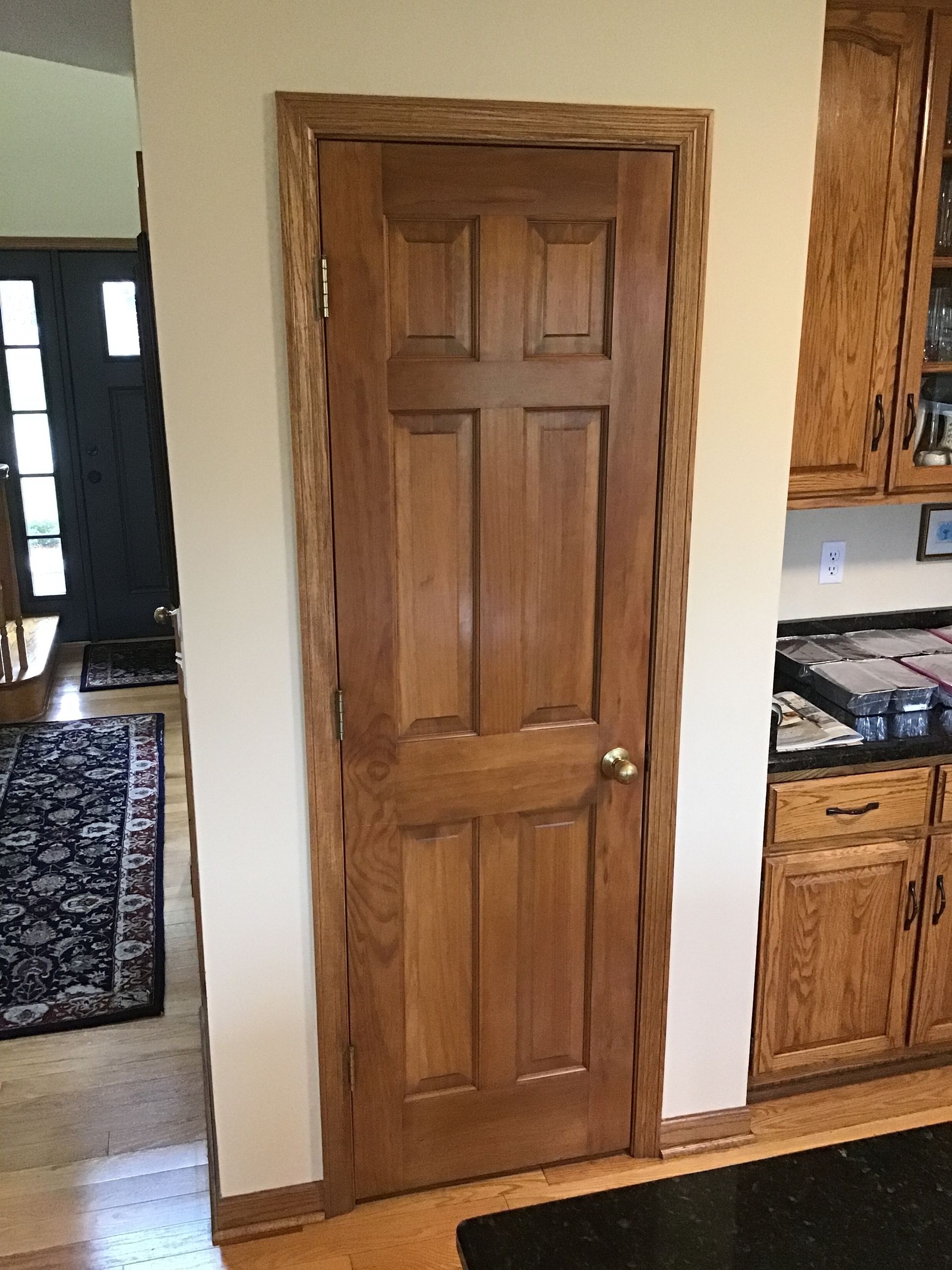 Wooden pantry door in a kitchen beside oak cabinets and a doorway to a hallway