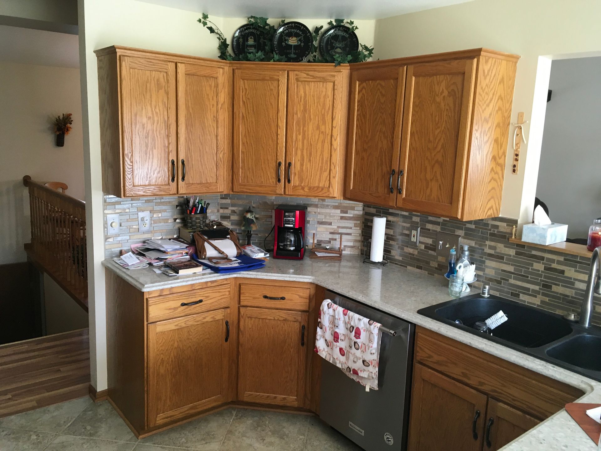 Small kitchen corner with oak cabinets, black sink, granite counter, and cluttered countertop.
