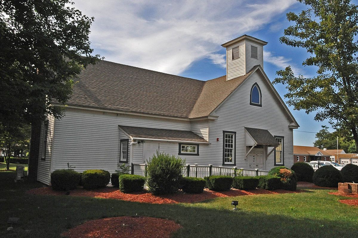 White clapboard church with a brown roof and a small bell tower on a sunny day.