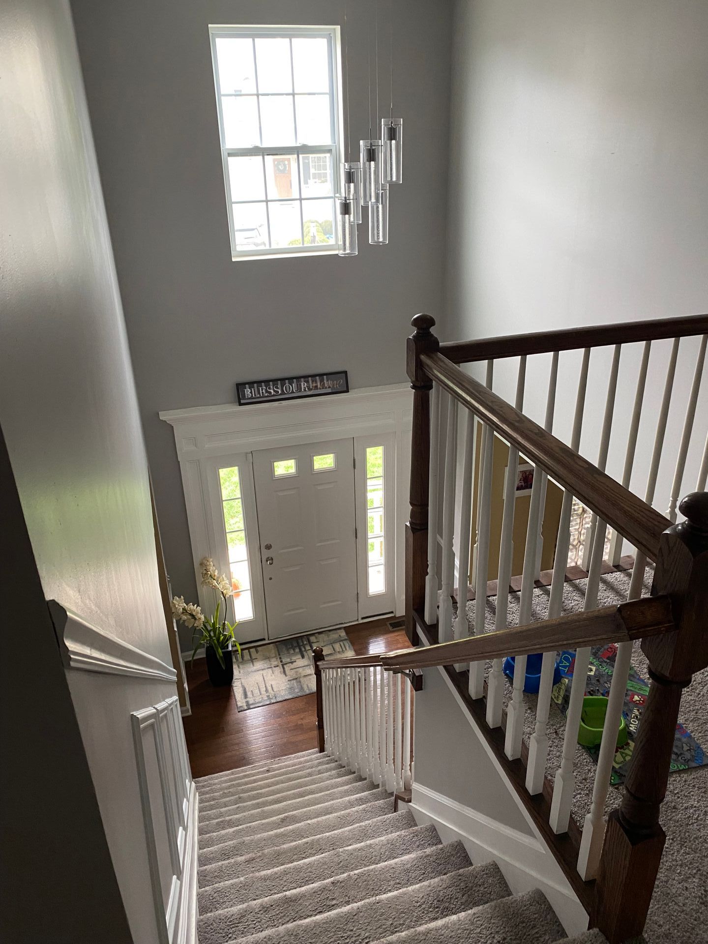 Stairwell with a view of an entryway, light gray walls, wooden stairs, white banister, front door with window.