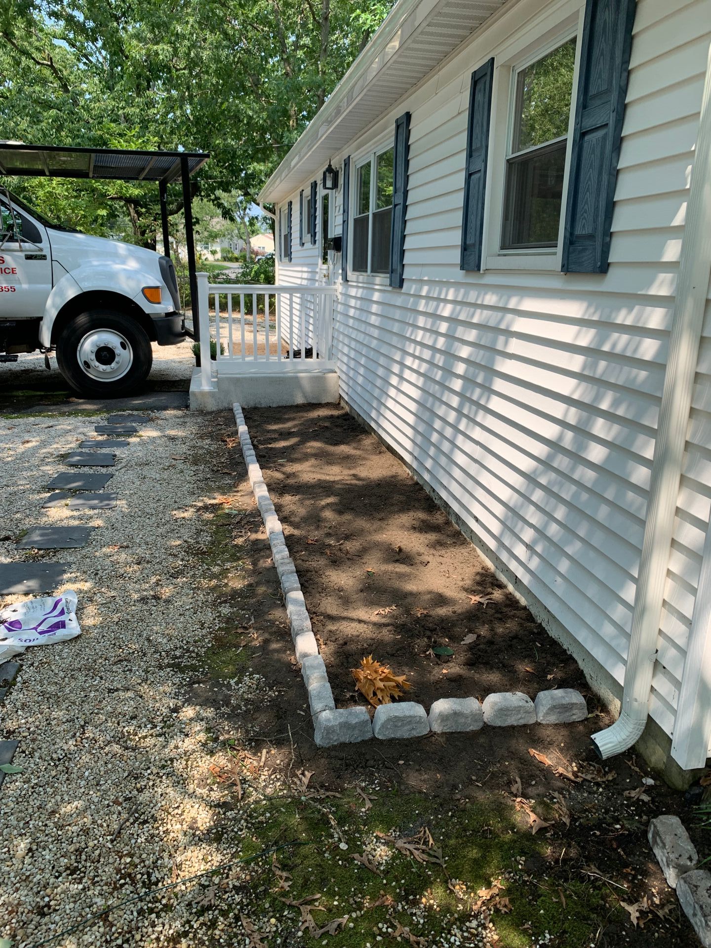 White house with blue shutters, a new garden bed with gray edging, and a gravel walkway.