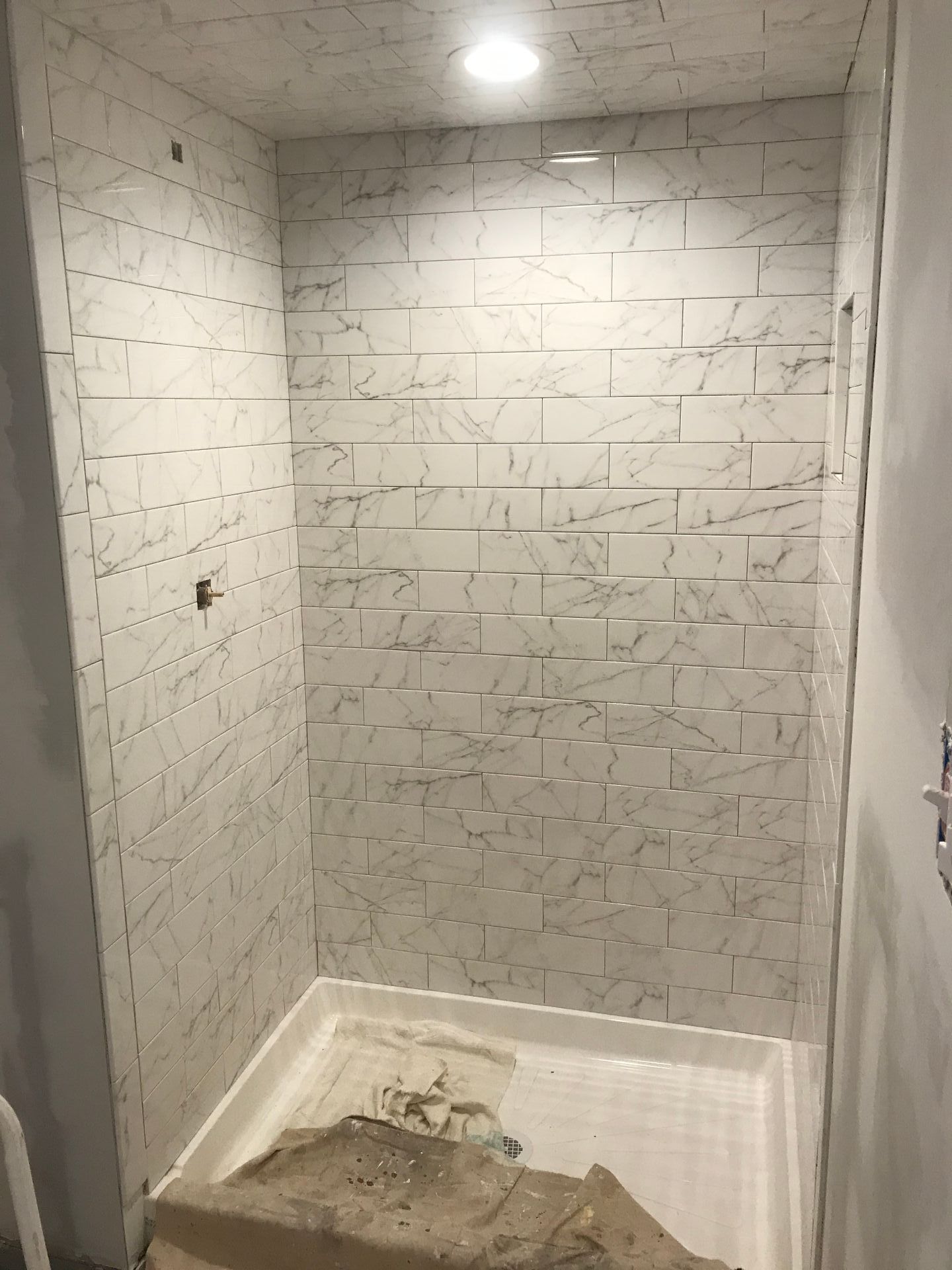 Shower with white textured tile walls, glass door, and white shower pan.