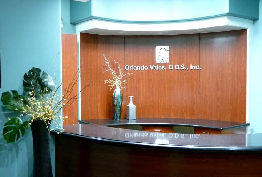 Reception desk at Orlando Wales, D.D.S., Inc., with a brown wooden backdrop, flowers, and a sleek black counter.