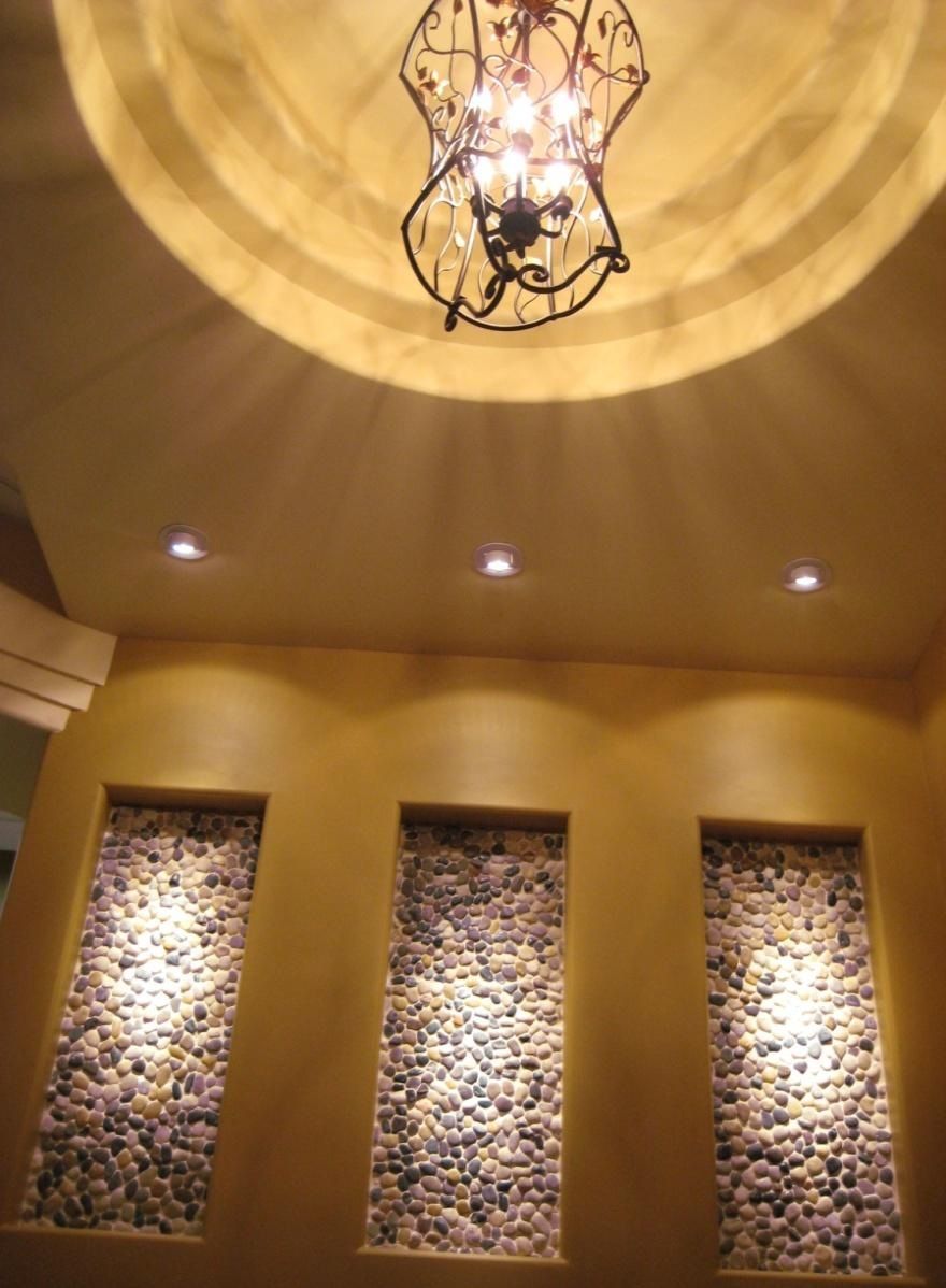 Three illuminated stone niches in a gold-colored wall, with a chandelier and circular ceiling fixture above.
