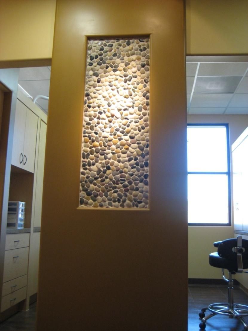 Brown wall with rectangular opening filled with small river stones; lit by spotlight.