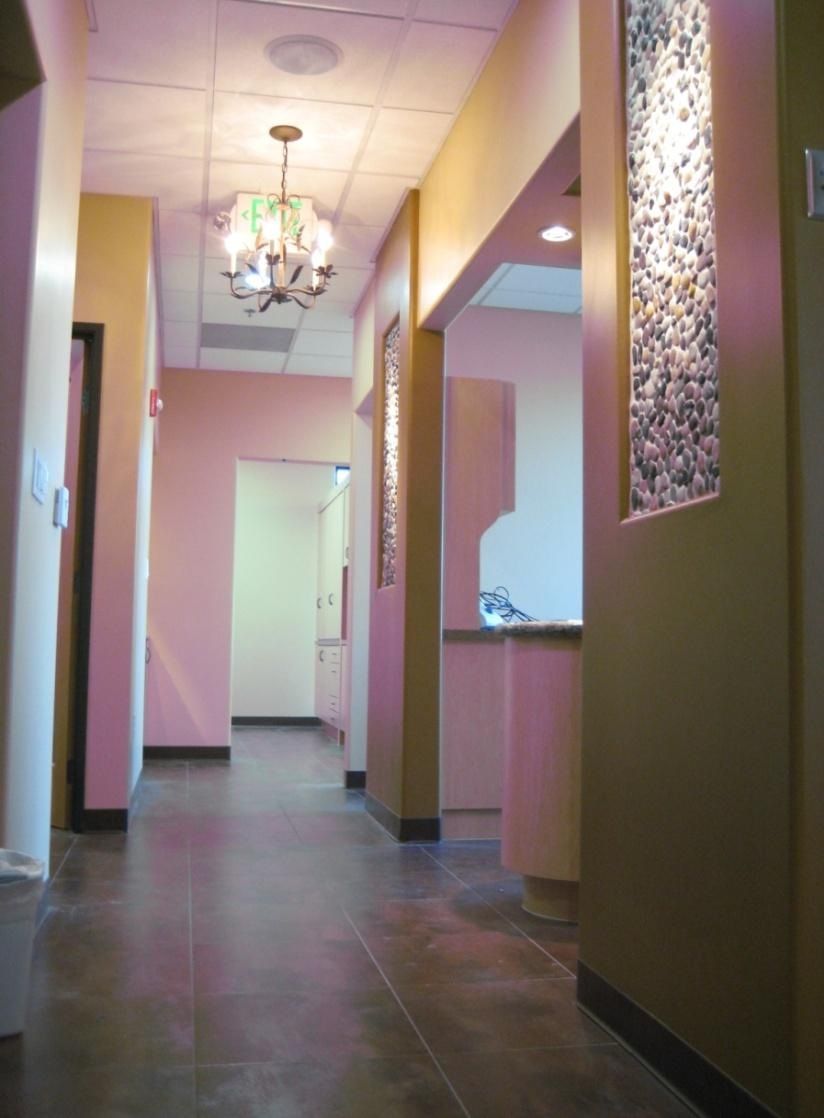 A narrow, well-lit hallway in a medical office, with decorative elements on the walls and a chandelier.