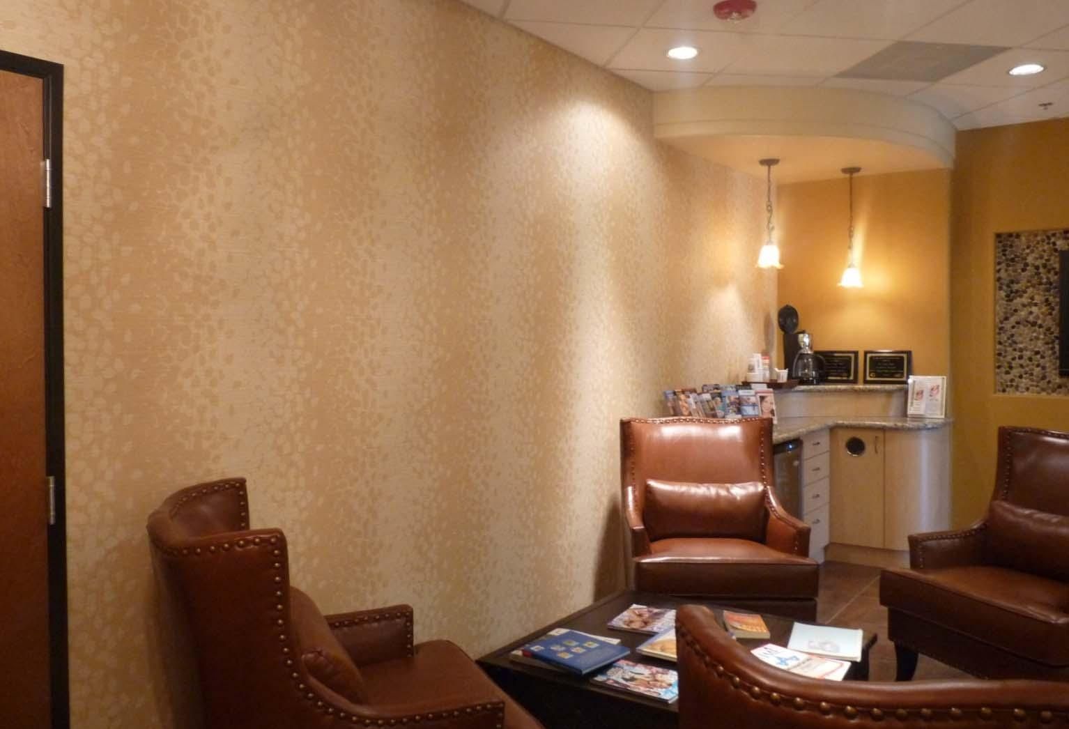 Waiting room with brown leather chairs, textured beige wall, and a small coffee station.