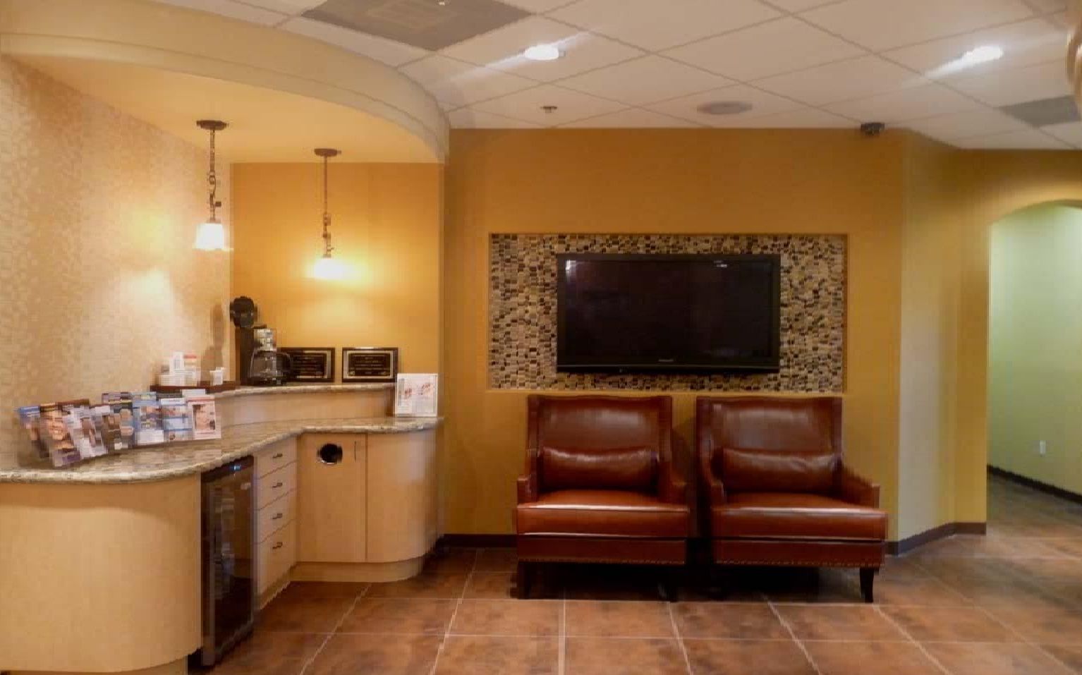 Waiting room with brown leather chairs, TV, and curved desk in a gold-toned room.