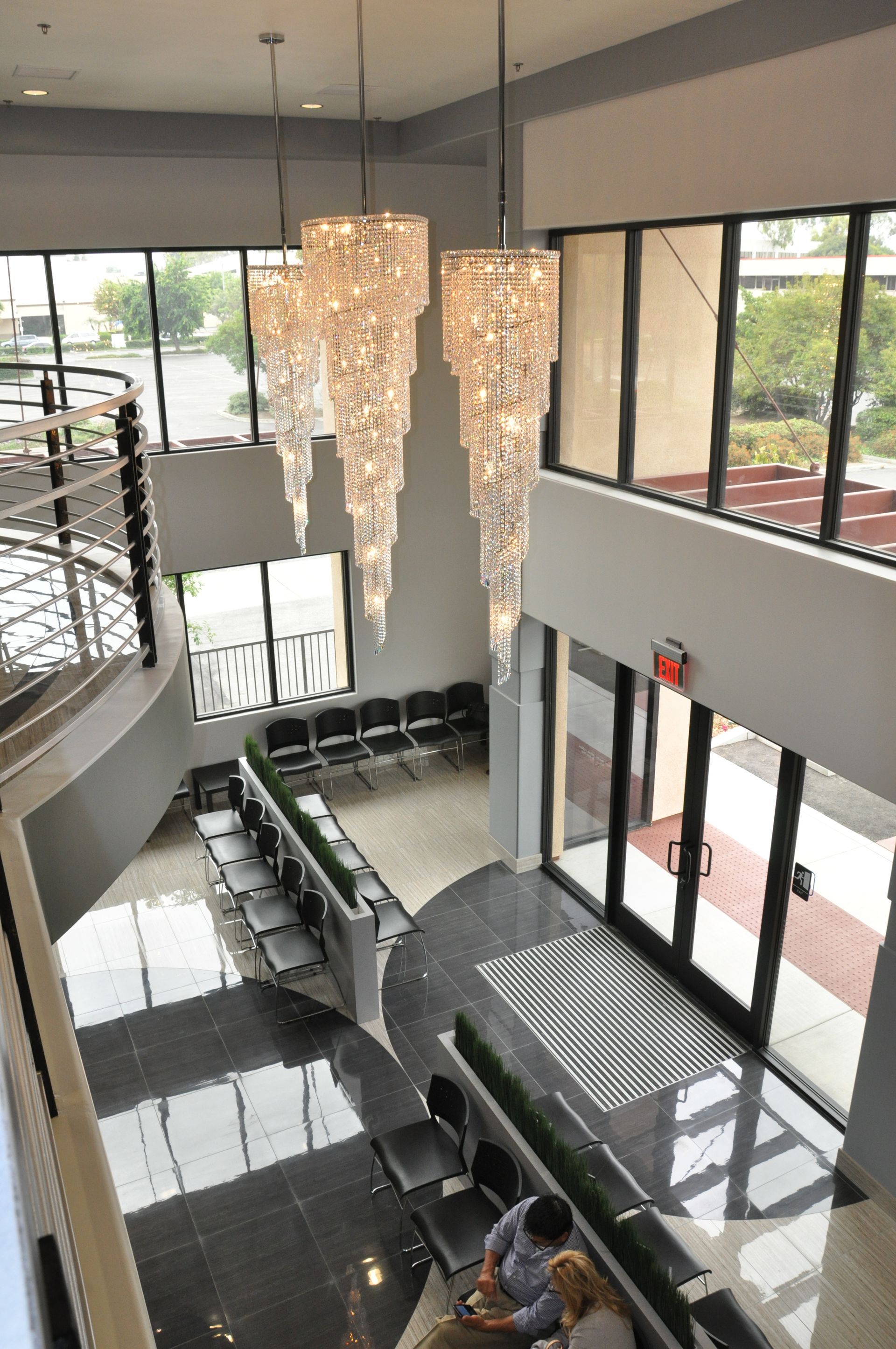 Elegant, bright two-story lobby with black and white tiled floors, large chandeliers, and waiting area with seating.