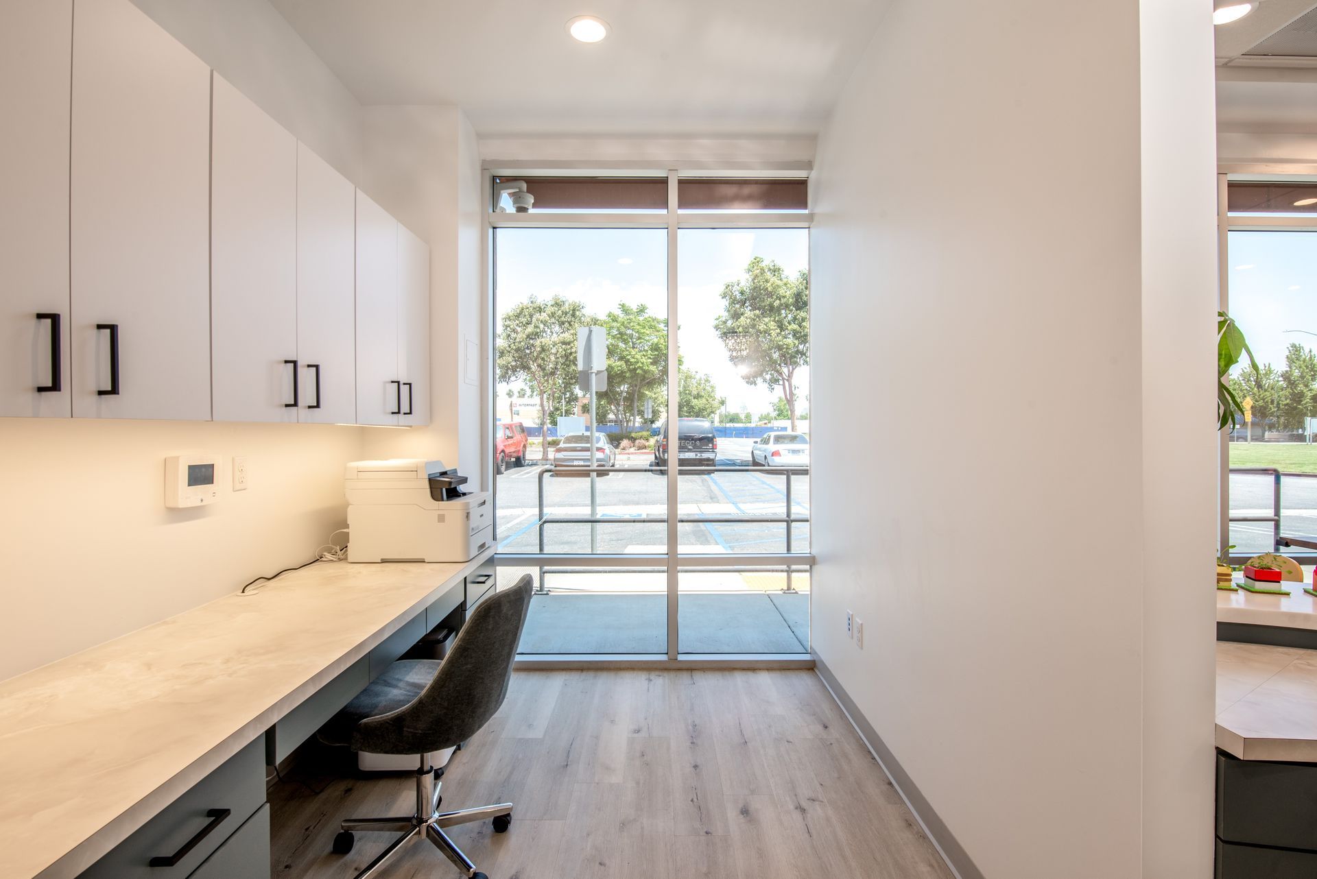 Office space with white cabinets, desk, chair, and large window overlooking a parking lot.