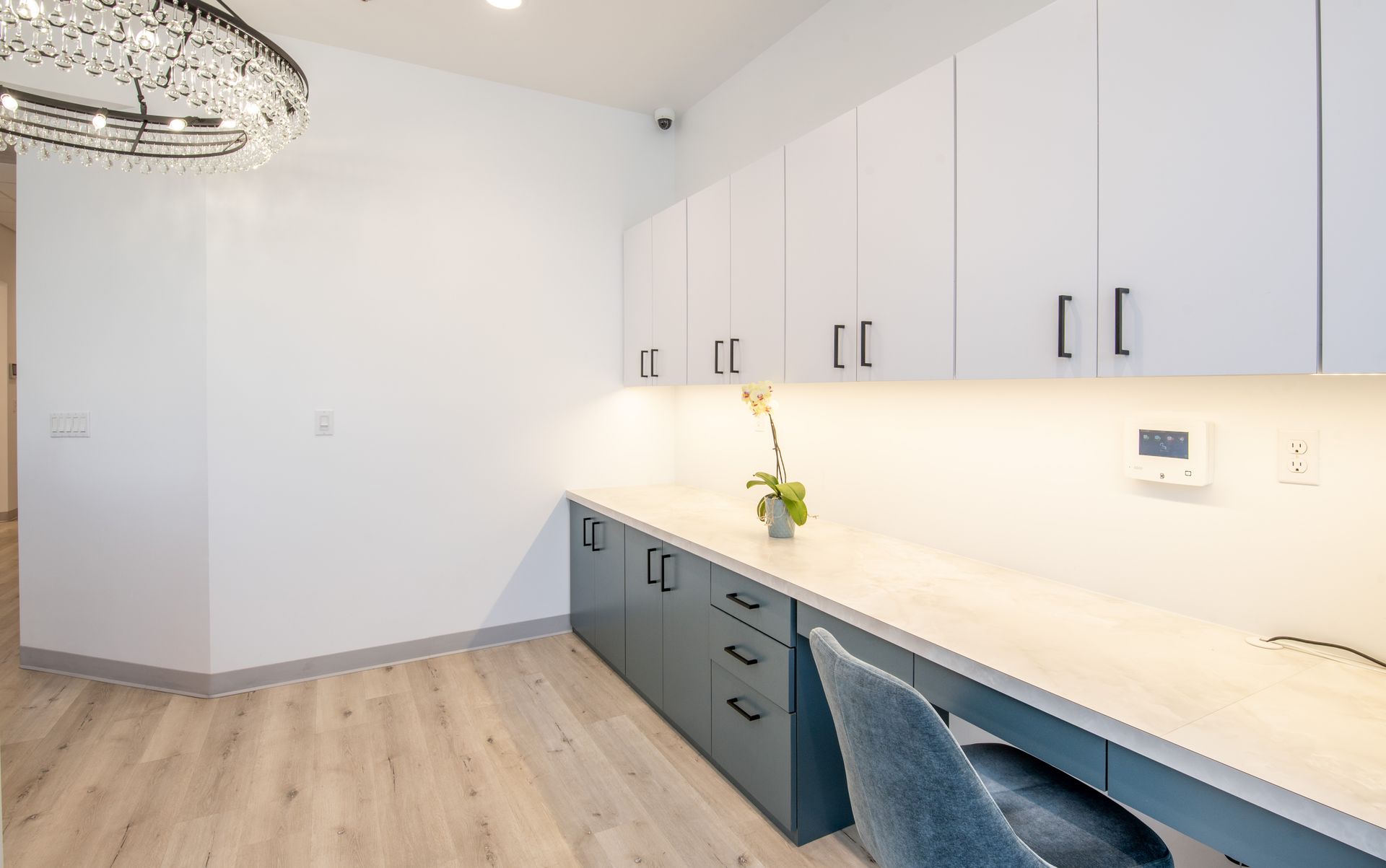 Modern office with white cabinetry, gray desk, and a decorative chandelier.