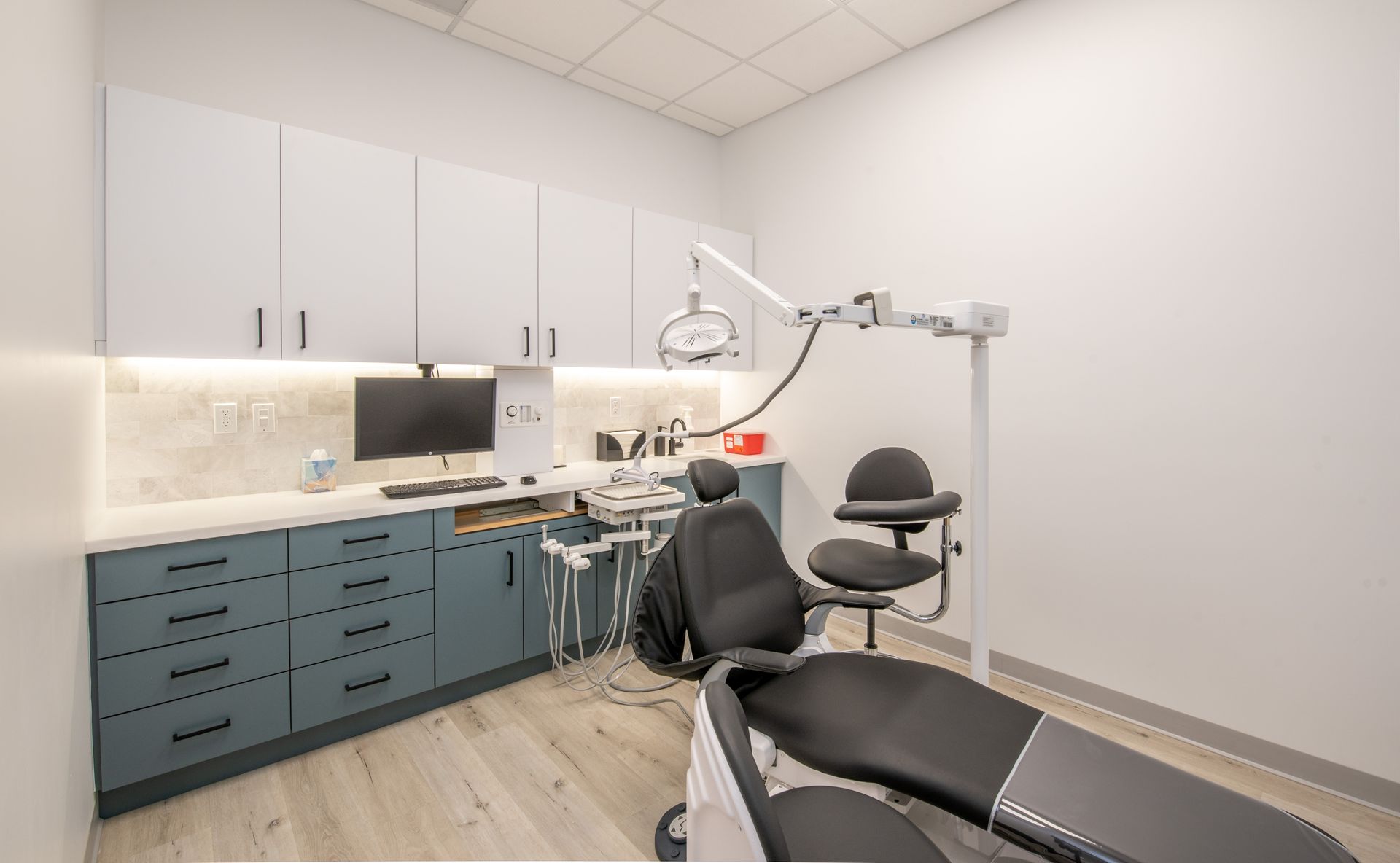 Dental operatory with blue-gray cabinets, dental chair, equipment, and computer.