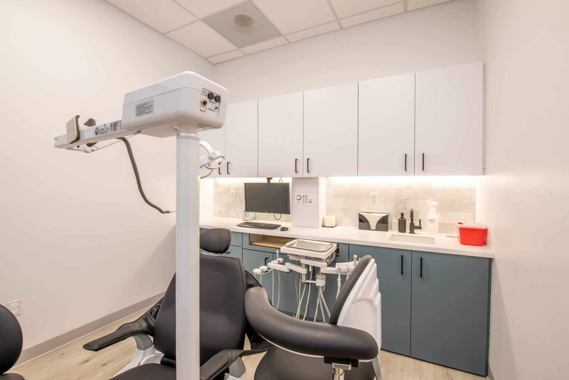 Dental office room with a chair, light, cabinets, sink, and computer.