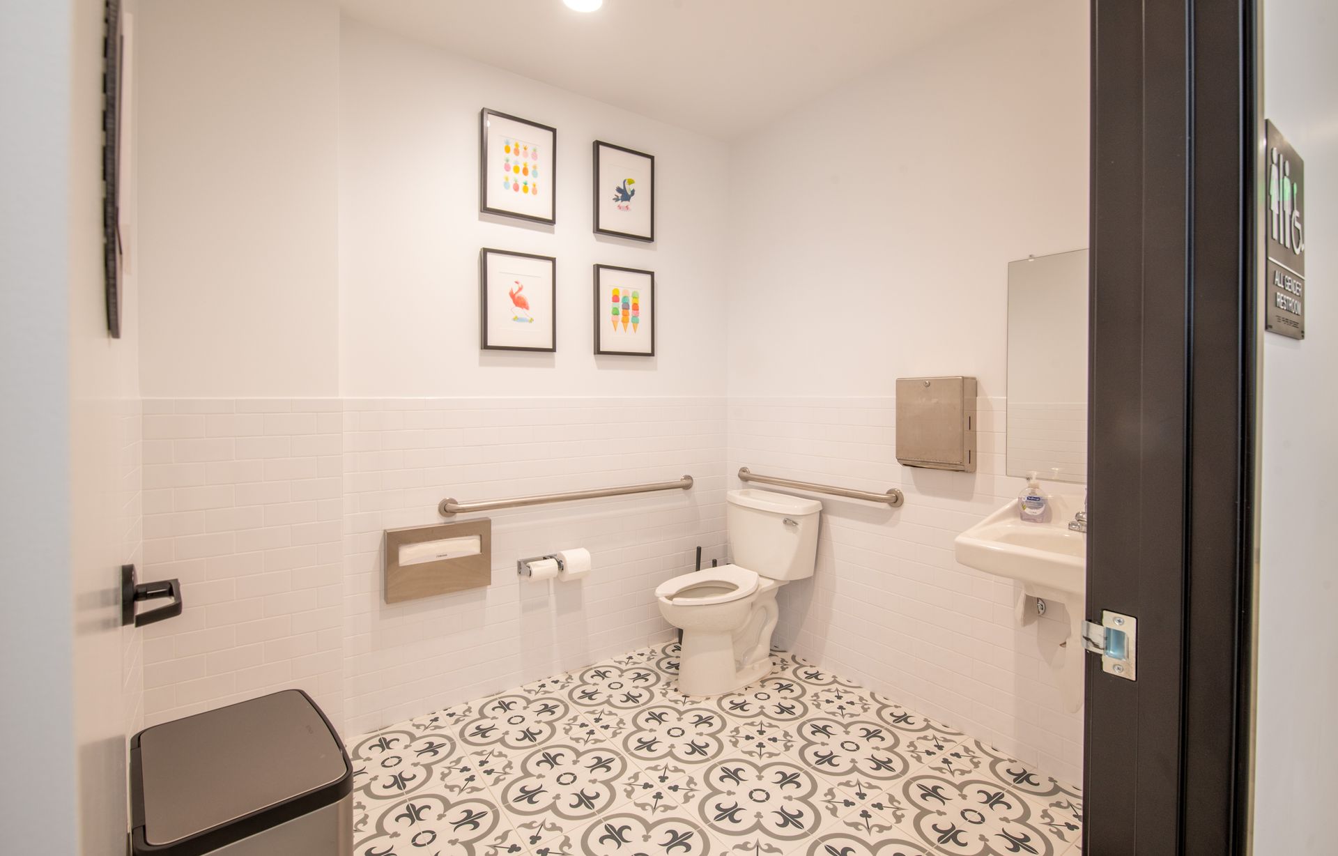 Bathroom with white walls, decorative floor, accessible toilet, and wall art.