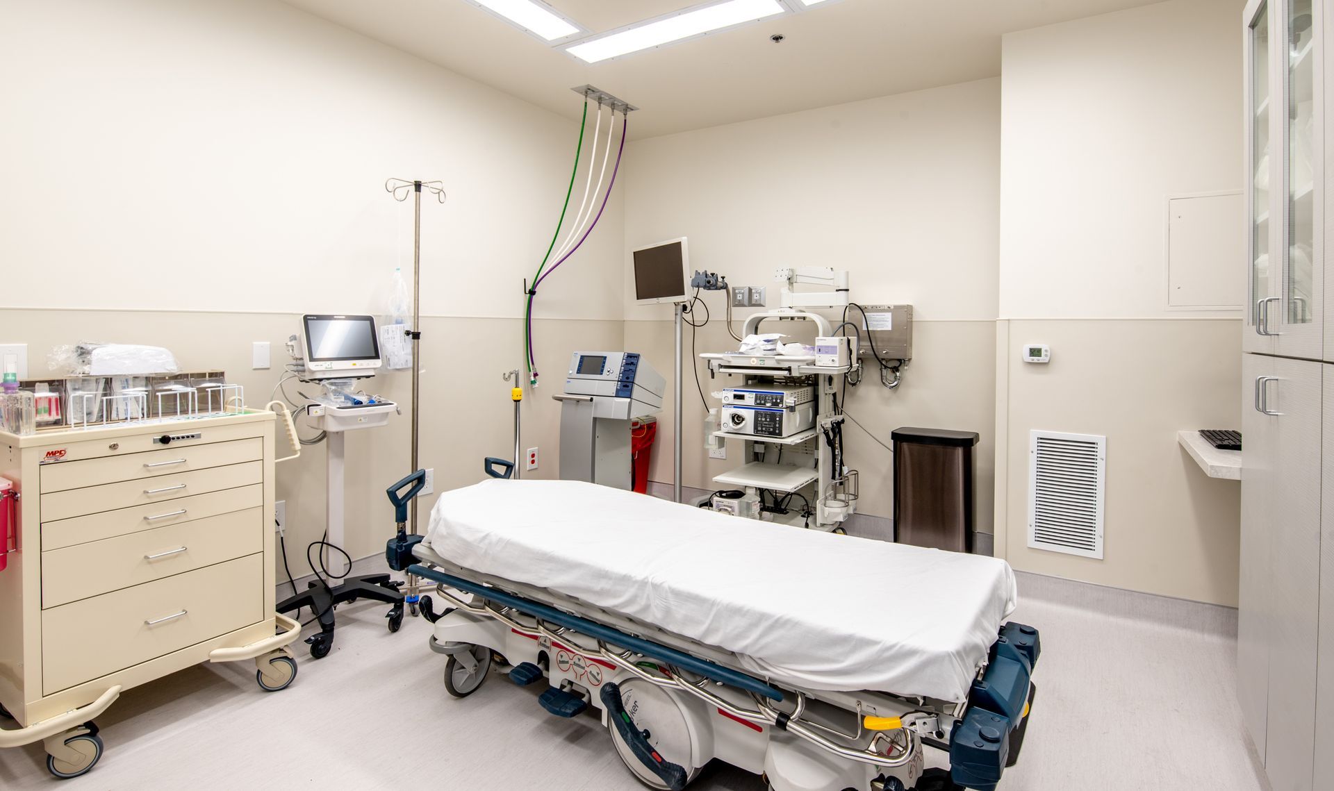 Empty hospital room with a bed, medical equipment, and a rolling cart.