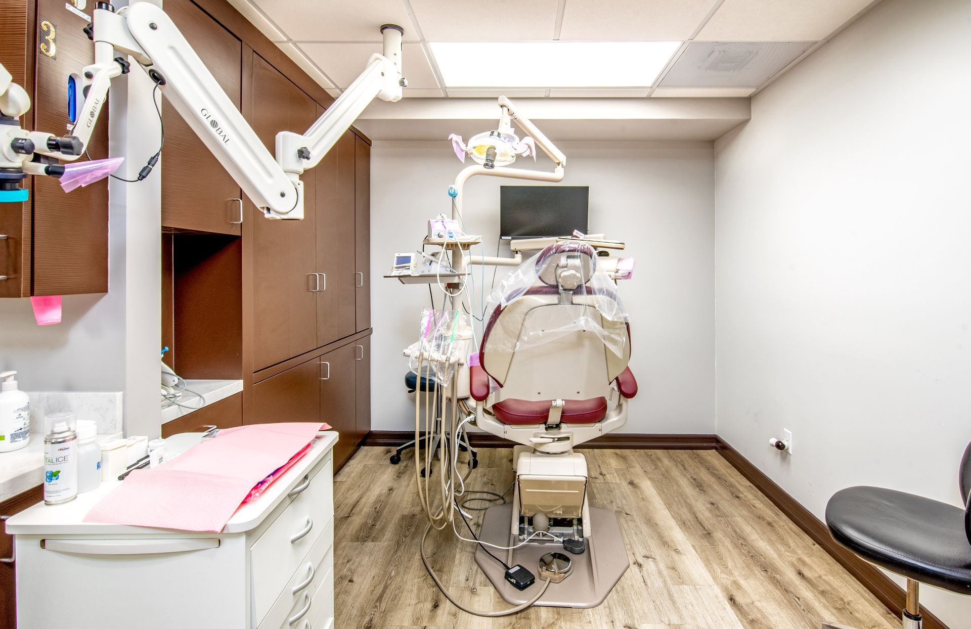 Dental office: patient chair, equipment, brown cabinets, light wood floors, and gray walls.