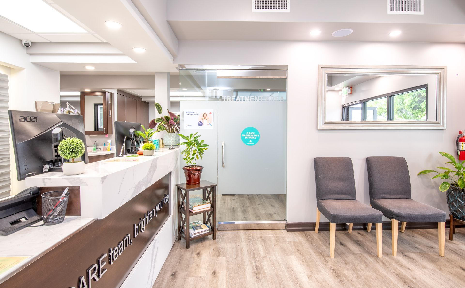 Modern dental office reception area with chairs, front desk, and glass door.