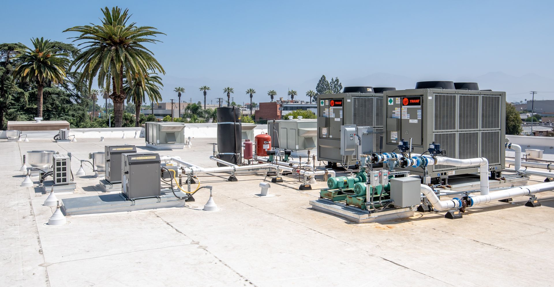 Rooftop with HVAC equipment under a clear blue sky; includes palm trees in the background.