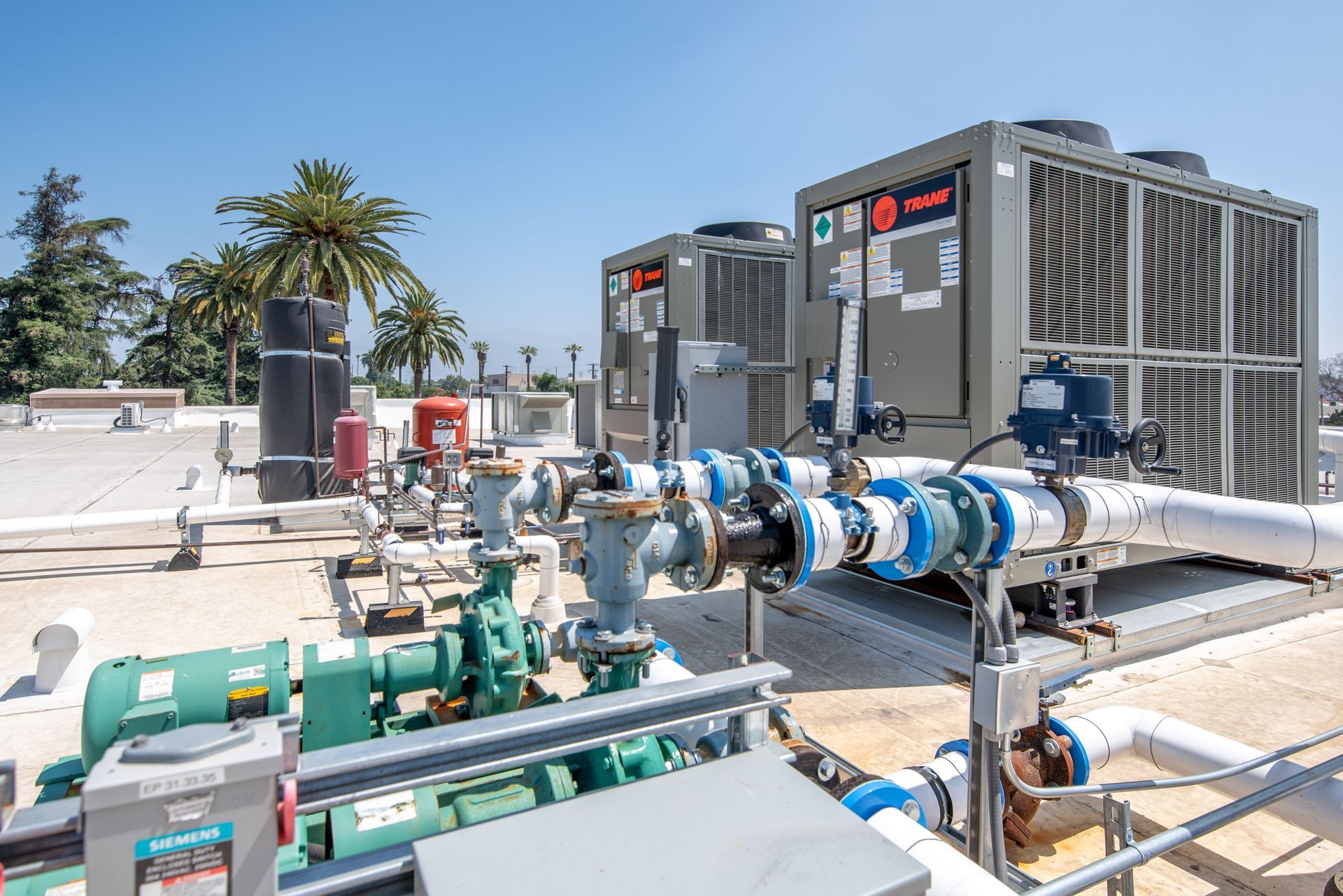 HVAC equipment on a rooftop with pipes, valves, and a Trane unit under a blue sky.