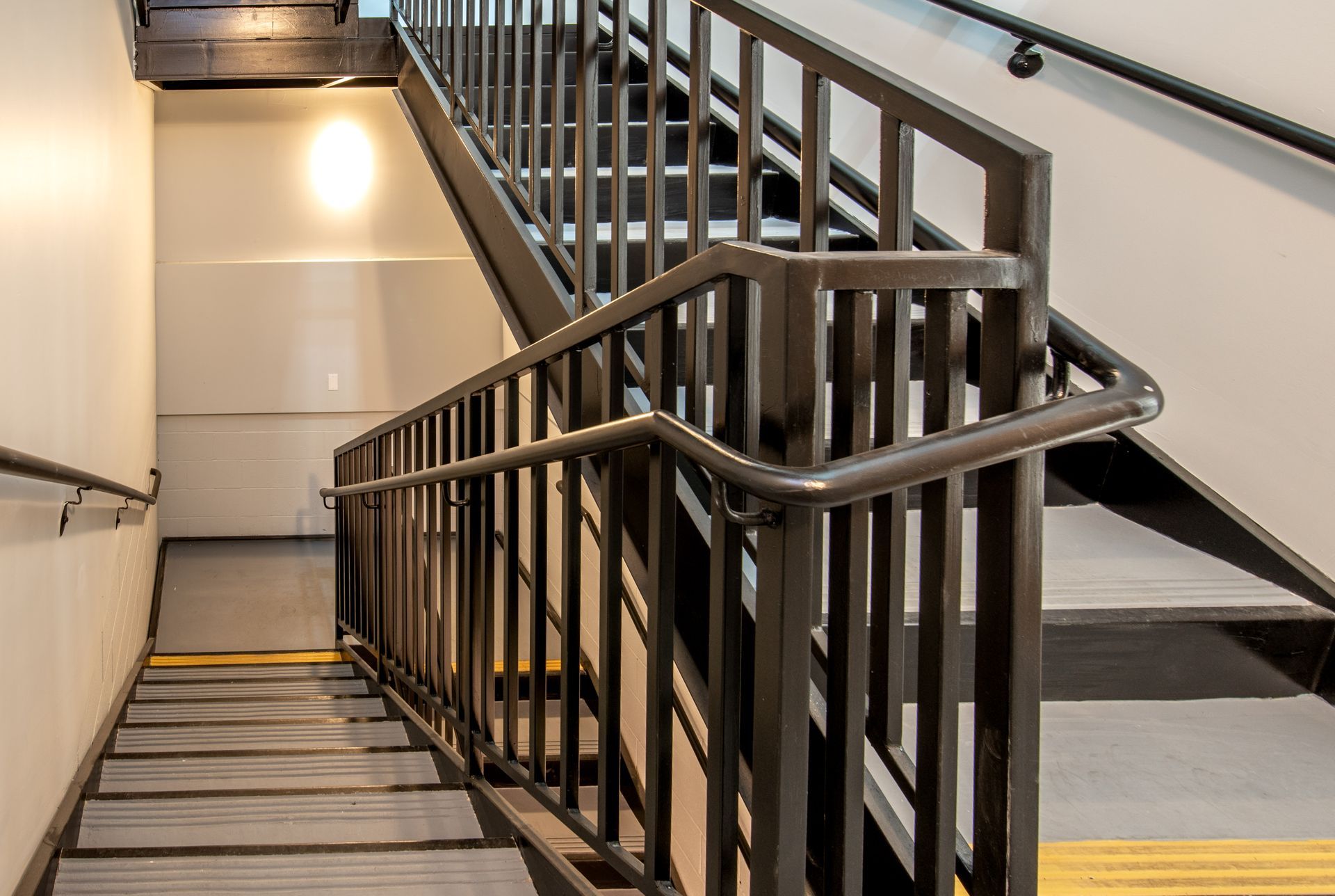 Indoor staircase with dark metal handrails and gray steps.
