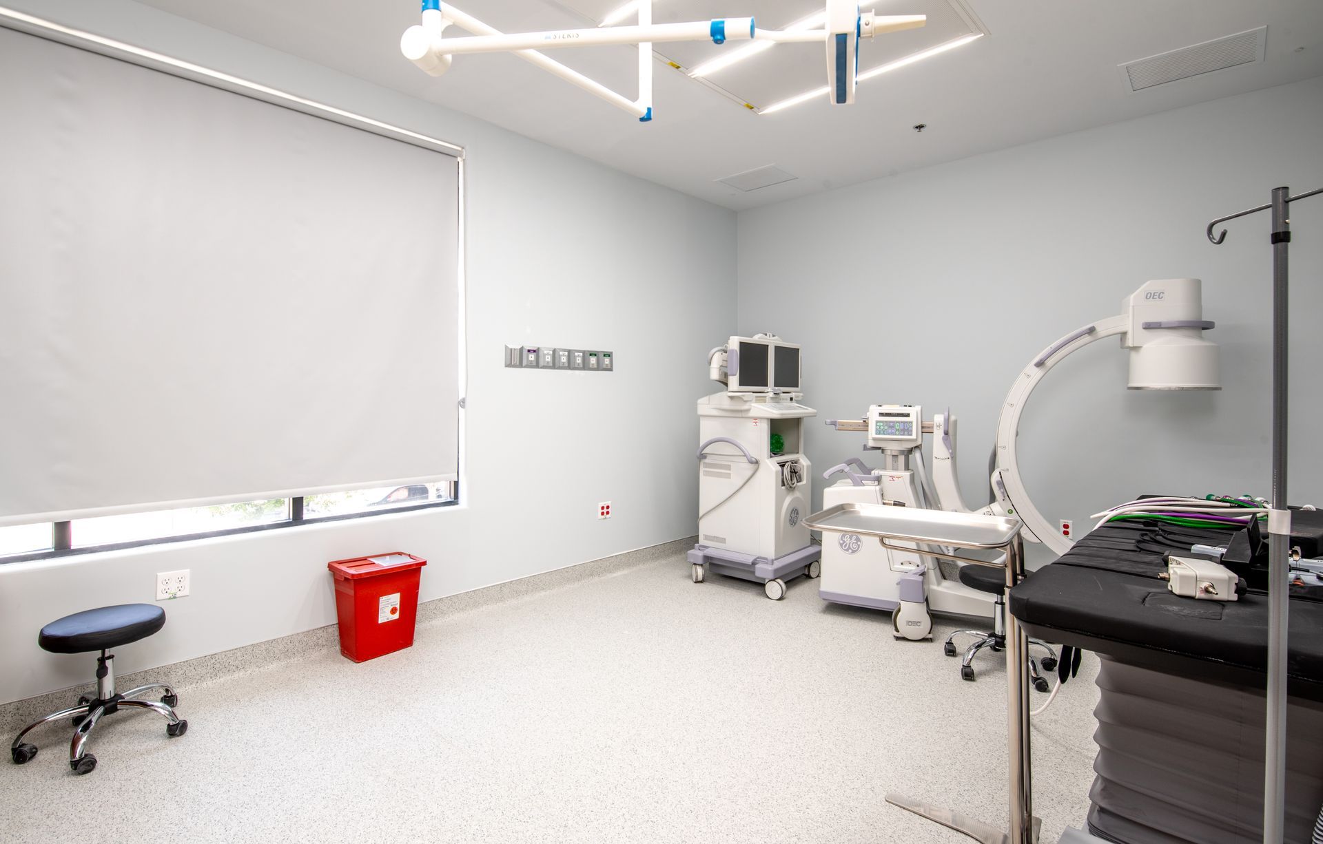 An operating room with medical equipment, including an X-ray machine, and a red waste bin.
