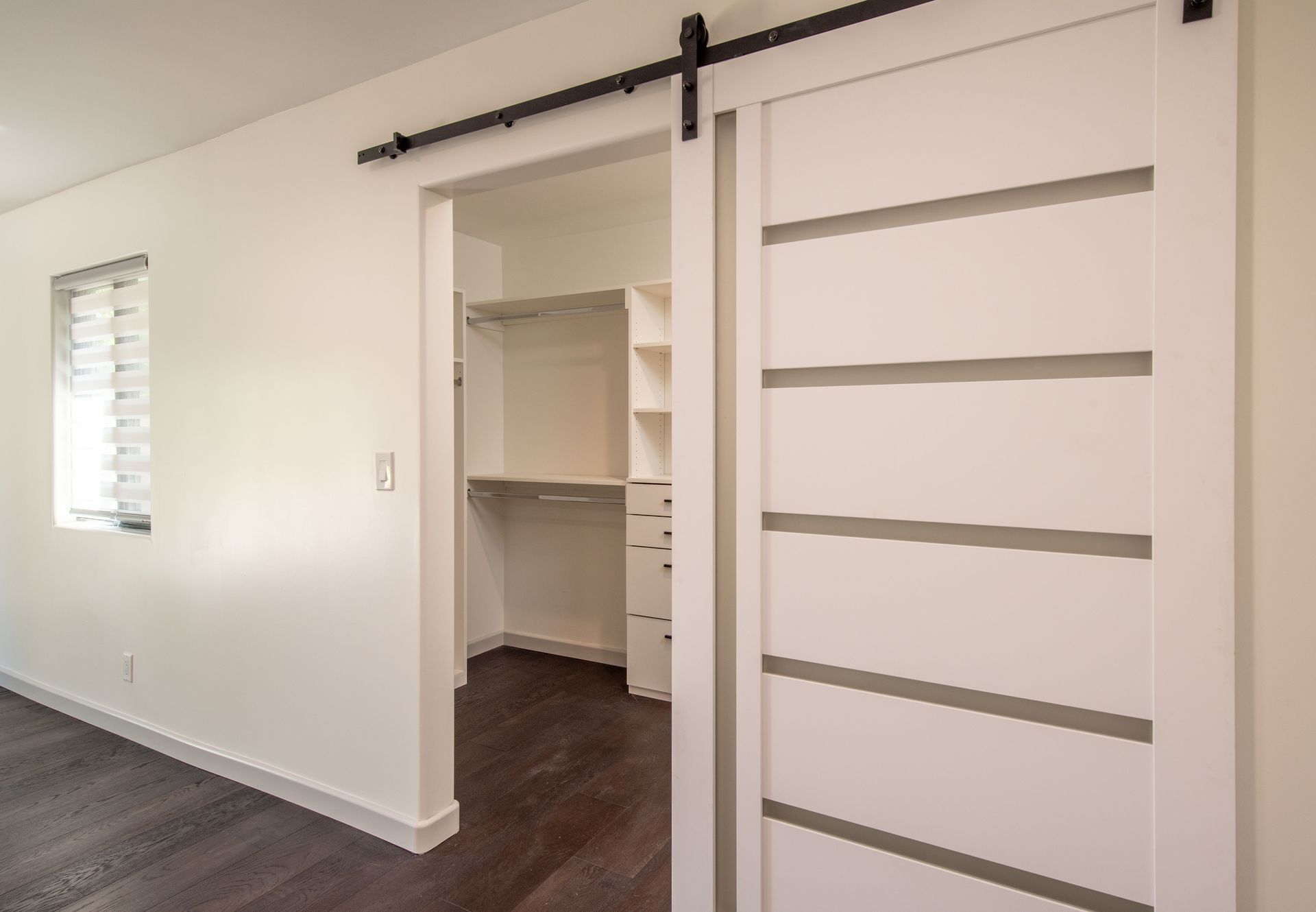 White bedroom with dark wood floor. A sliding barn door leads to a walk-in closet.