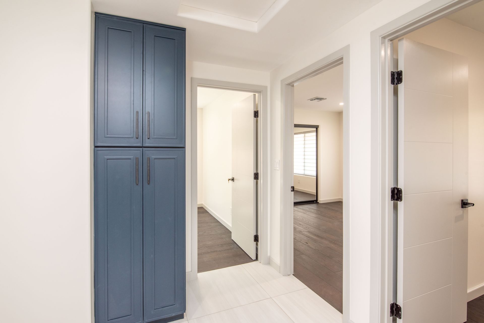 Hallway with blue cabinet, white doors, and wood and tile flooring.
