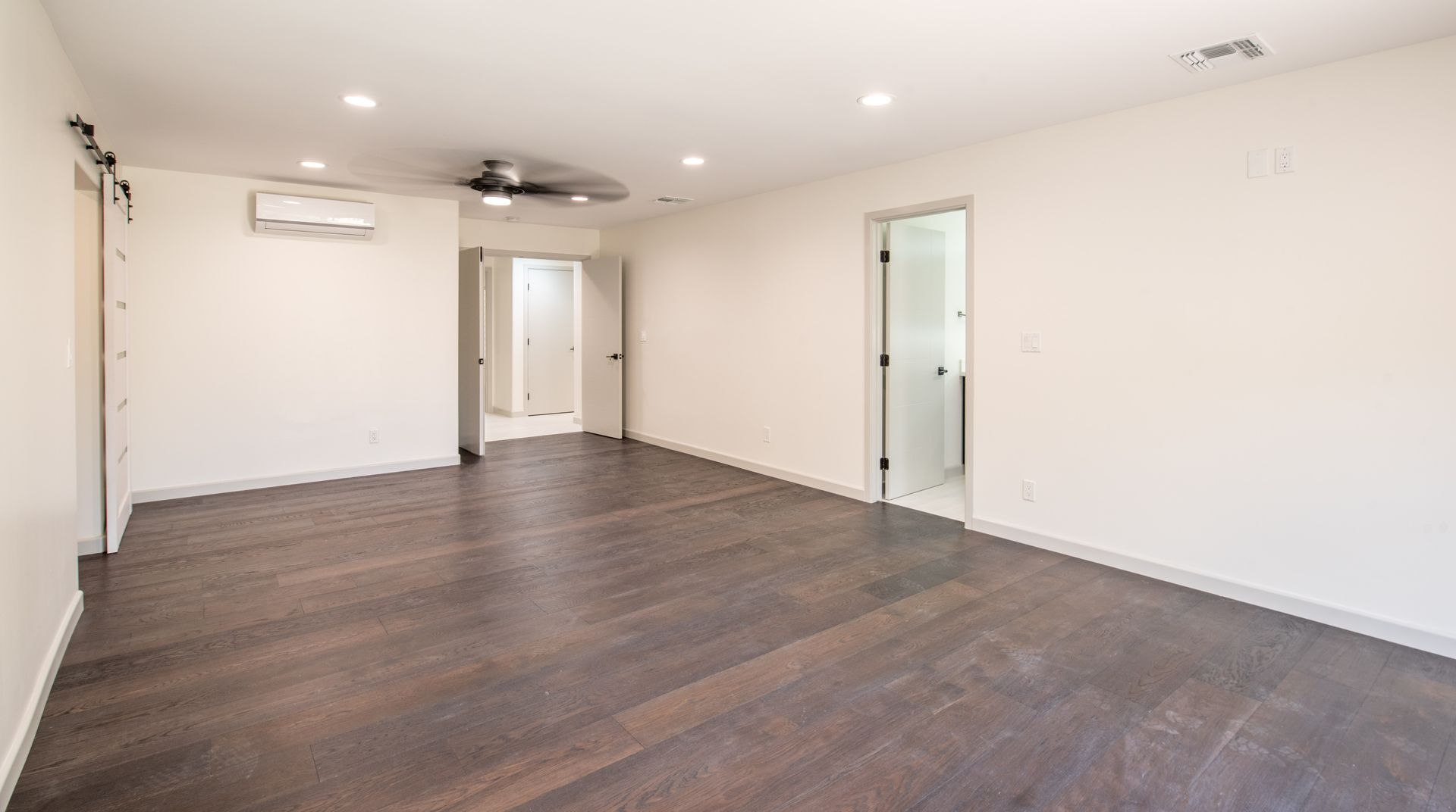 Empty room with dark wood floor, white walls, and a ceiling fan.