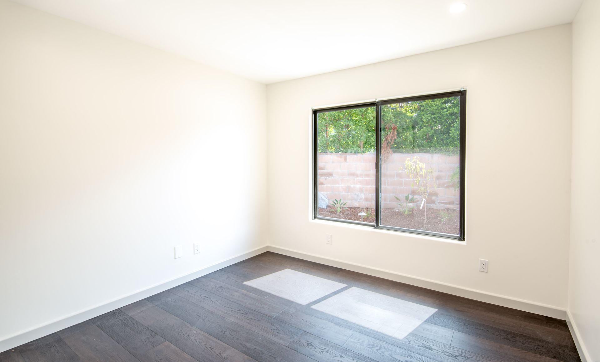 Empty room with dark wood floor, white walls, and a window.
