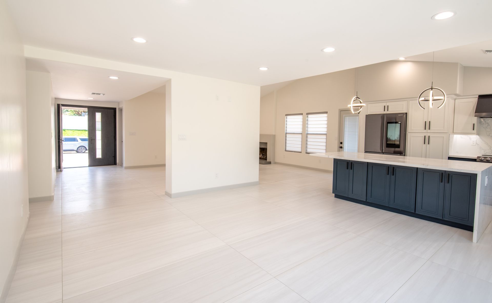 Bright interior with an open floor plan. Features a kitchen island, grey cabinets, and an entry door.