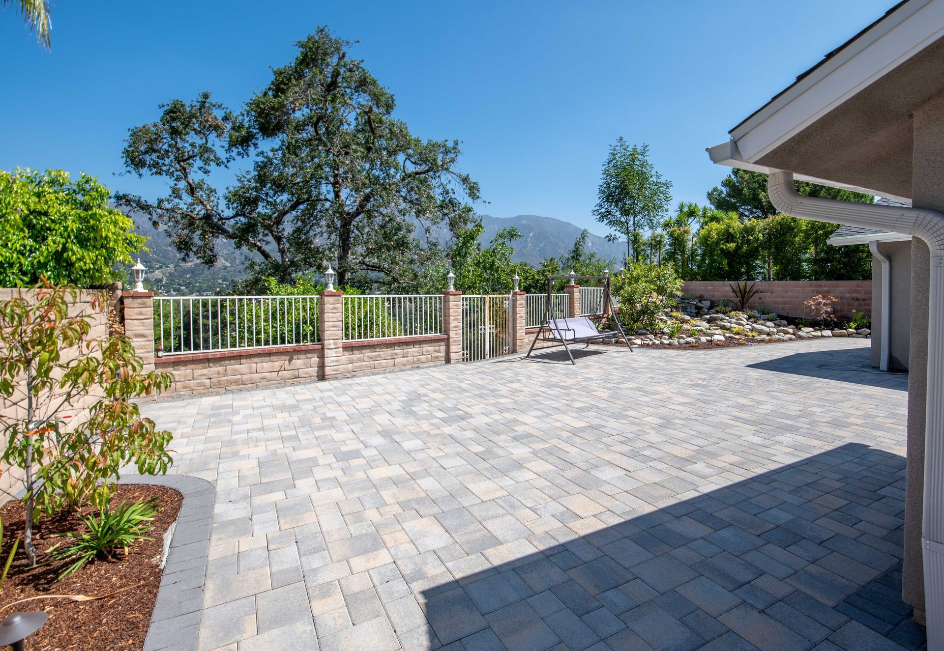 Patio with brickwork, white fence, and mountain view under a blue sky.
