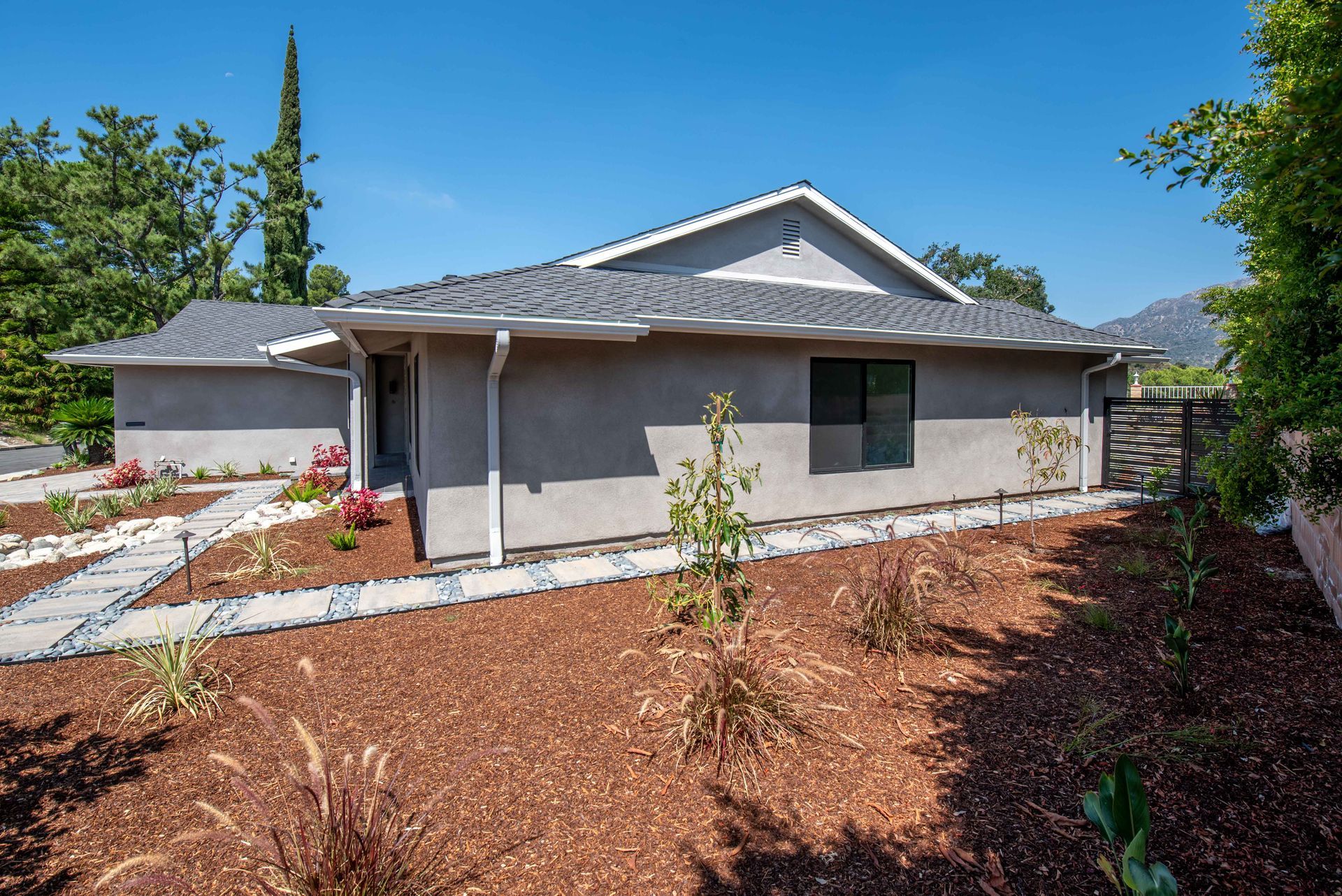 Single-story gray house with landscaping, blue sky, and mountain backdrop.