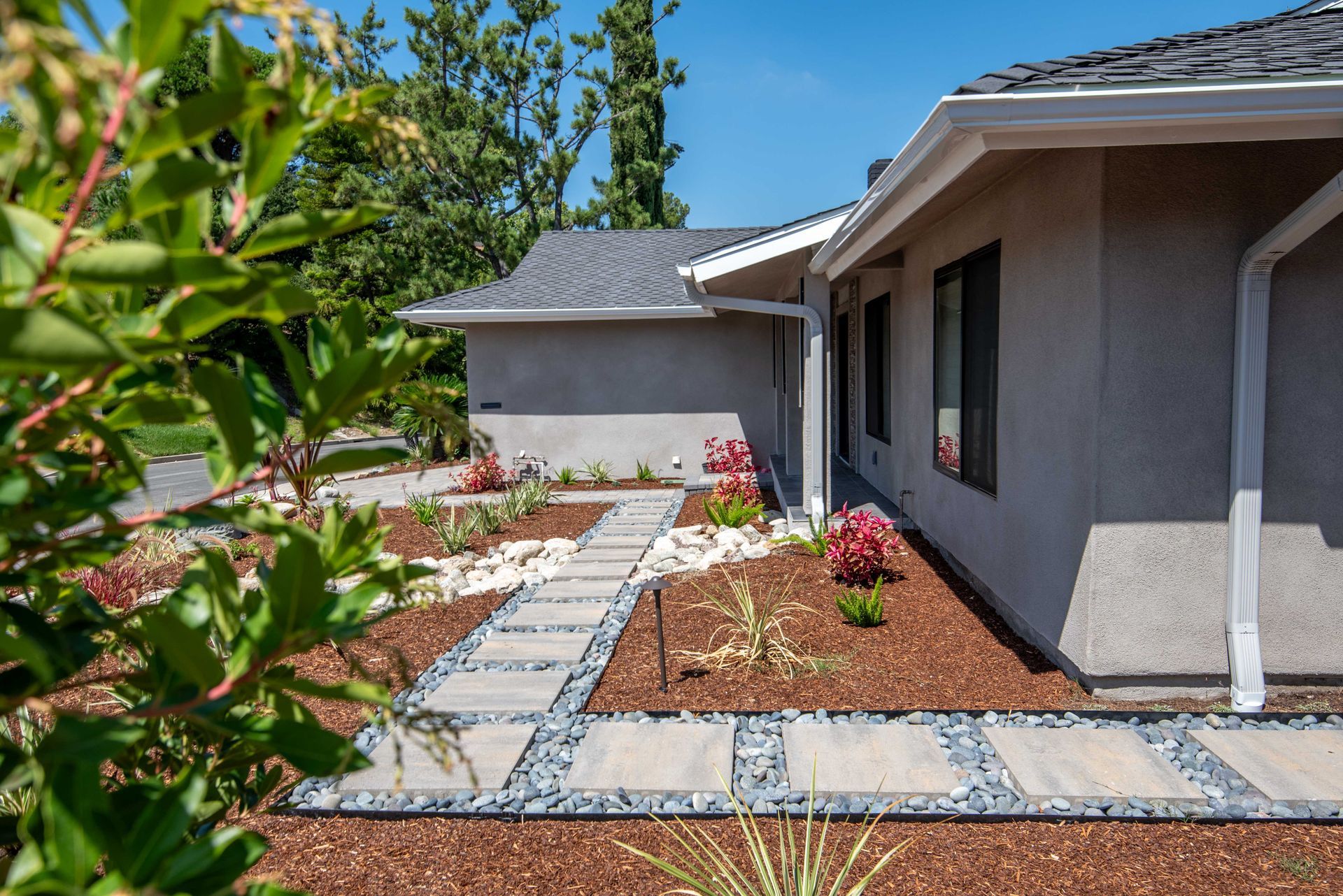 Stone walkway leading to a gray house with landscaping. Sunny day.