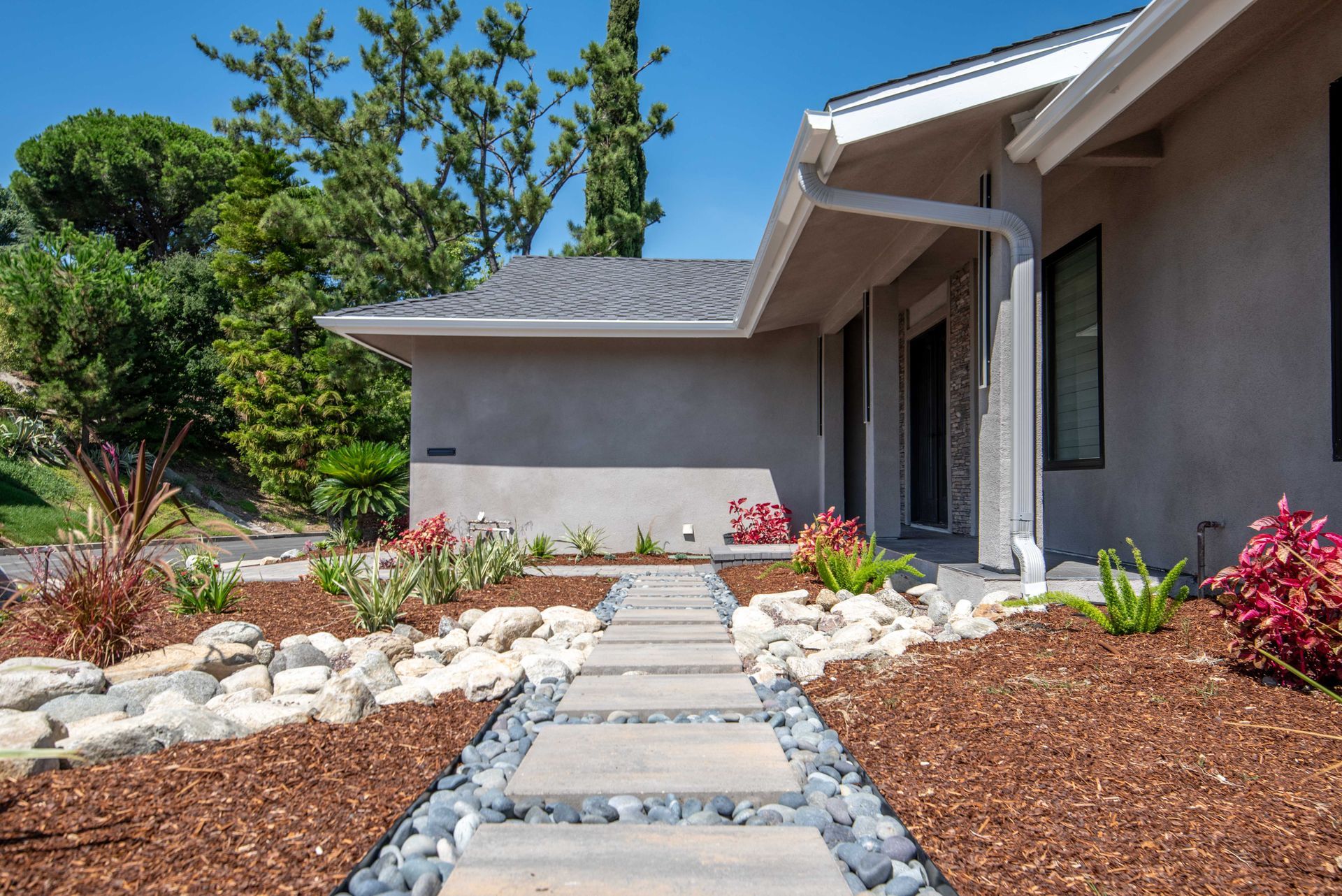 Stone pathway leading to a gray house with a landscaped front yard.