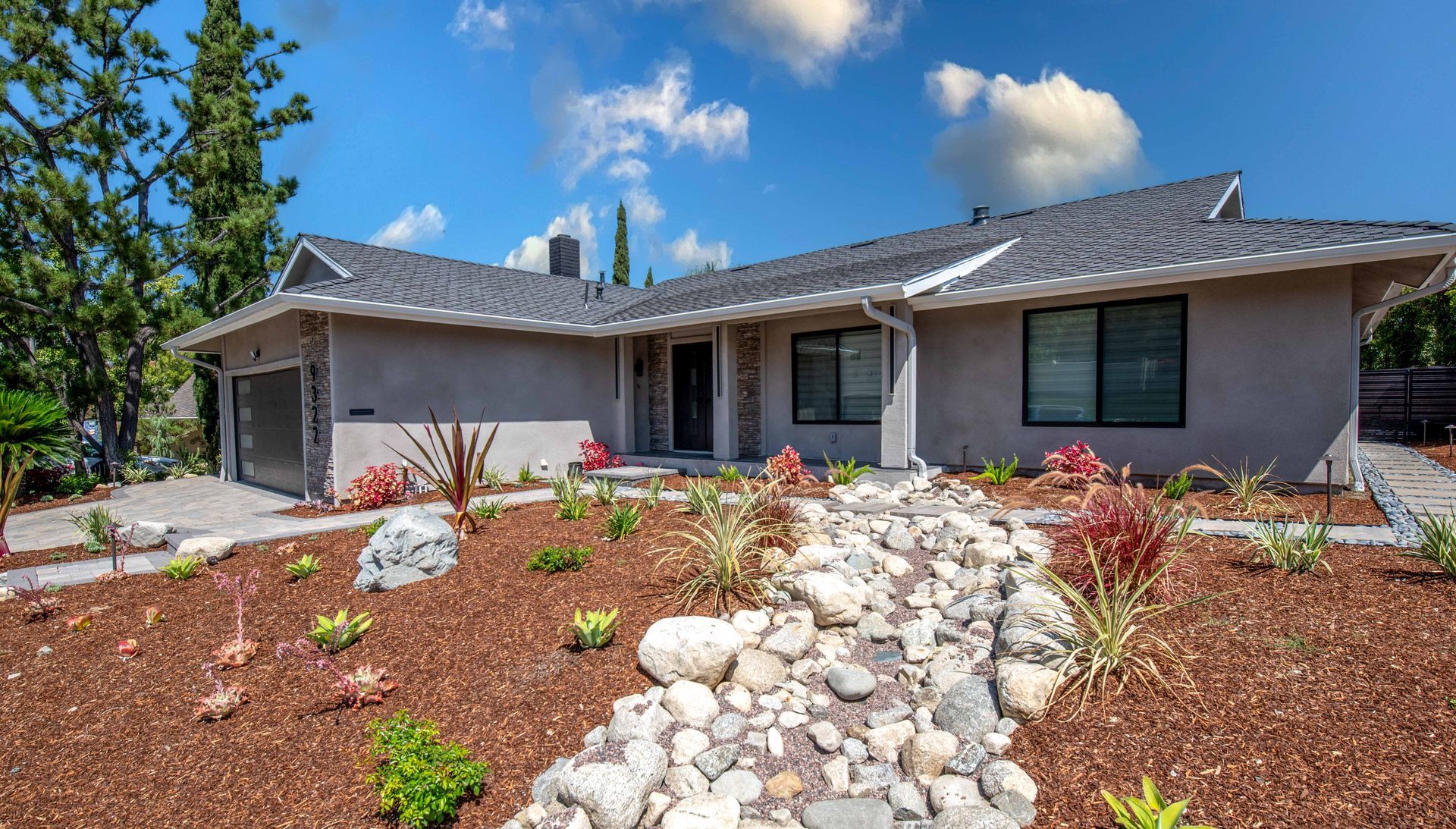 Ranch-style home with a rock-lined pathway, landscaped yard, and blue sky.