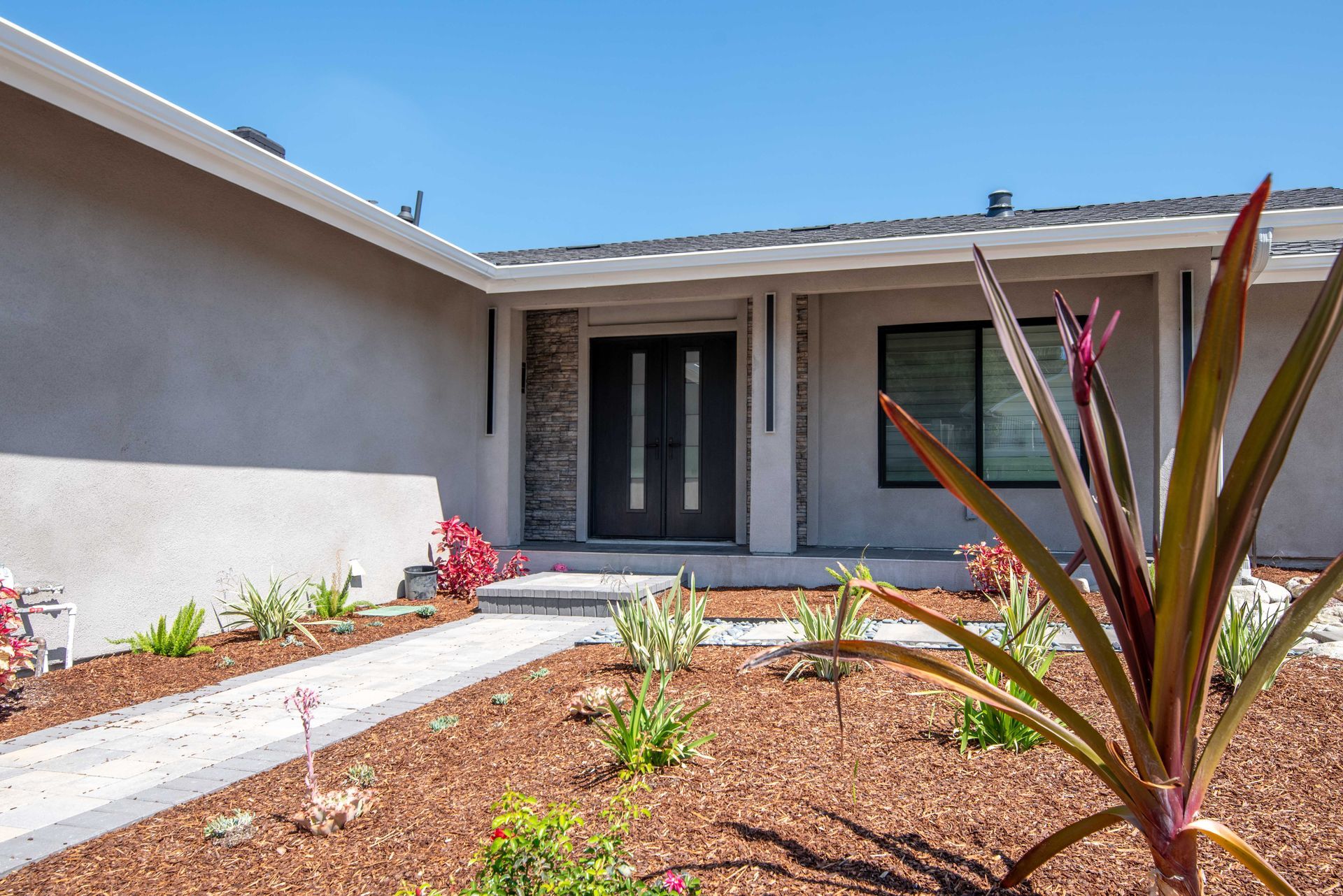 Ranch-style house exterior with landscaping and a pathway leading to the front door. Sunny day.