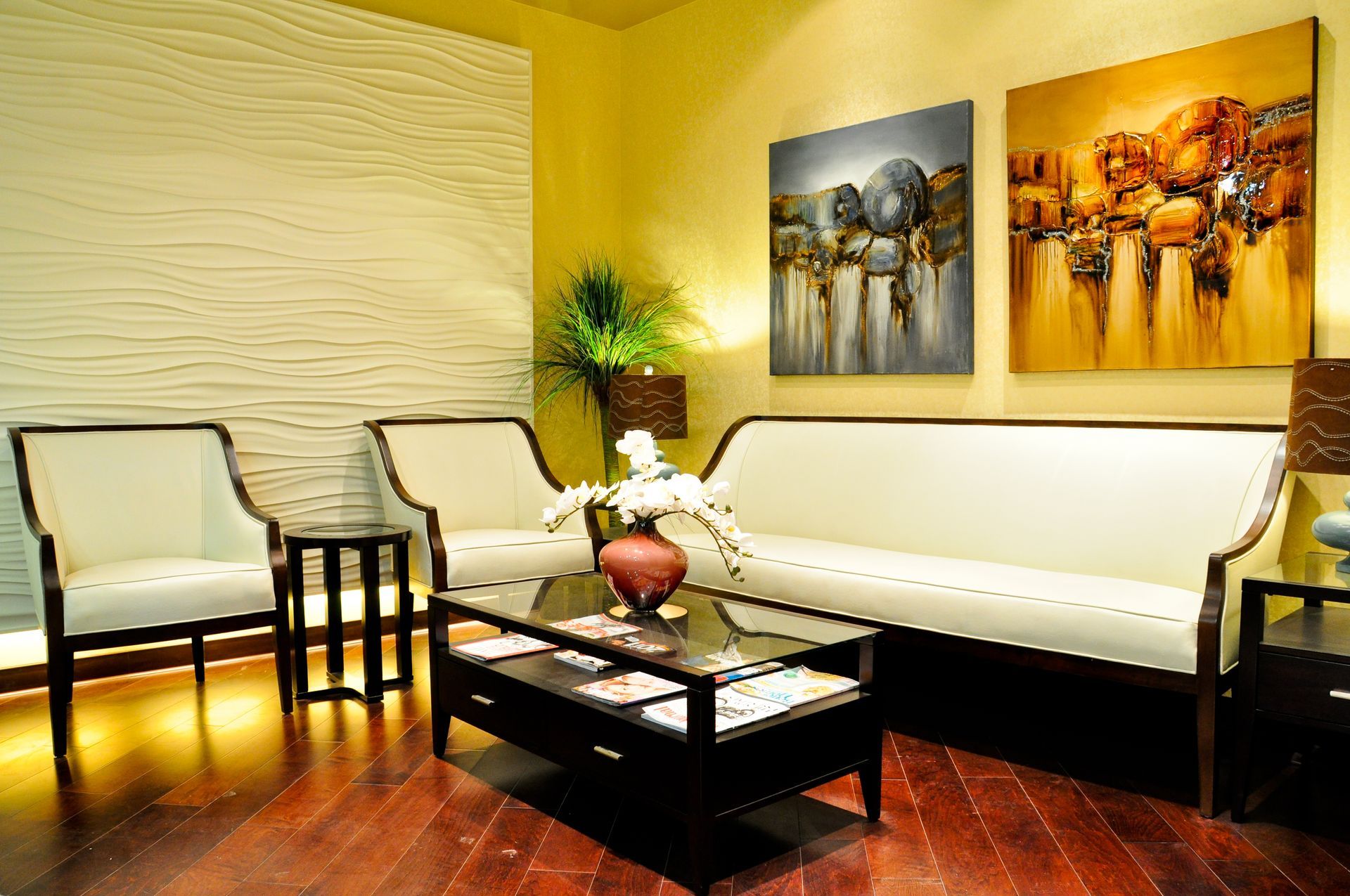 Waiting room with cream furniture, art, and a coffee table on a hardwood floor.
