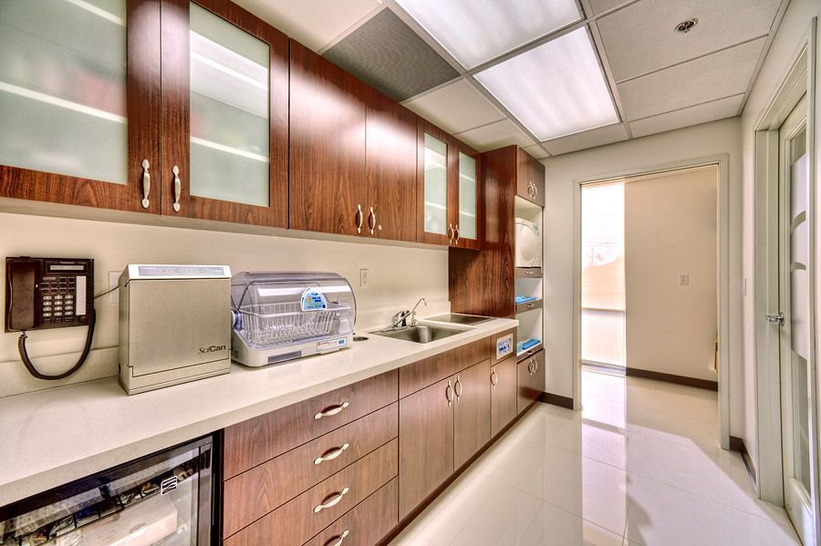 Dental office sterilization room with dark wood cabinetry, stainless steel sink, and medical equipment.