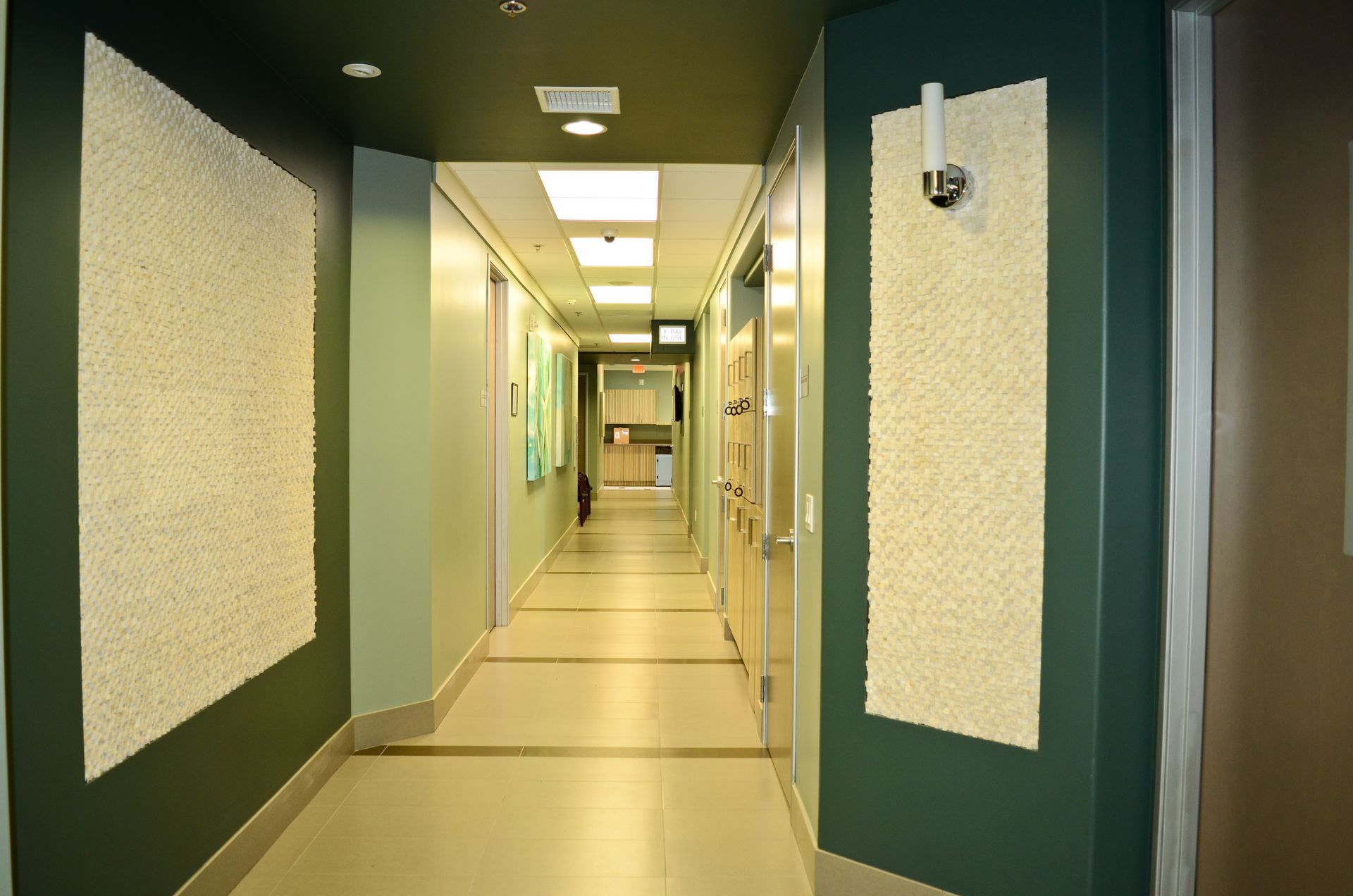 Hospital hallway with green walls, textured white panels, and doors.