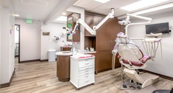 Dental office interior: dental chair, equipment, cabinets, light wood floor, exit door.