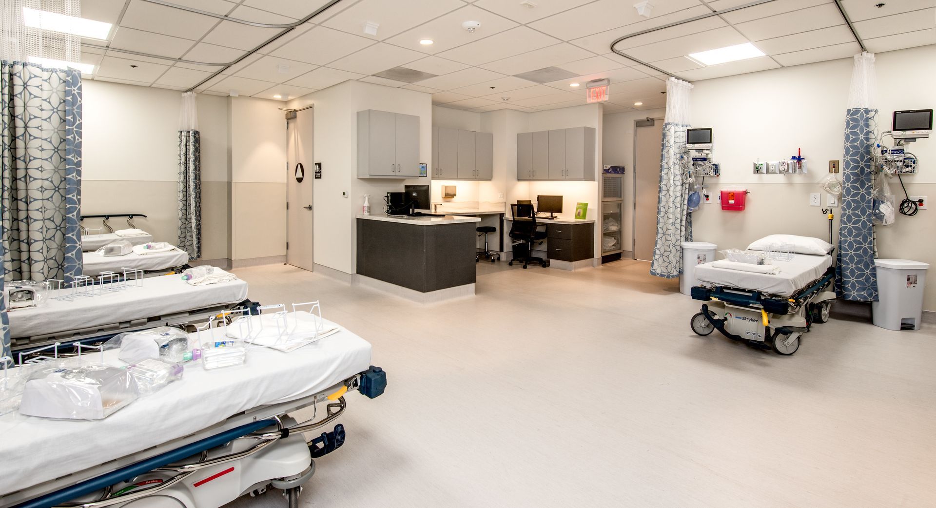 An empty hospital room with several beds, equipment, and a nursing station.