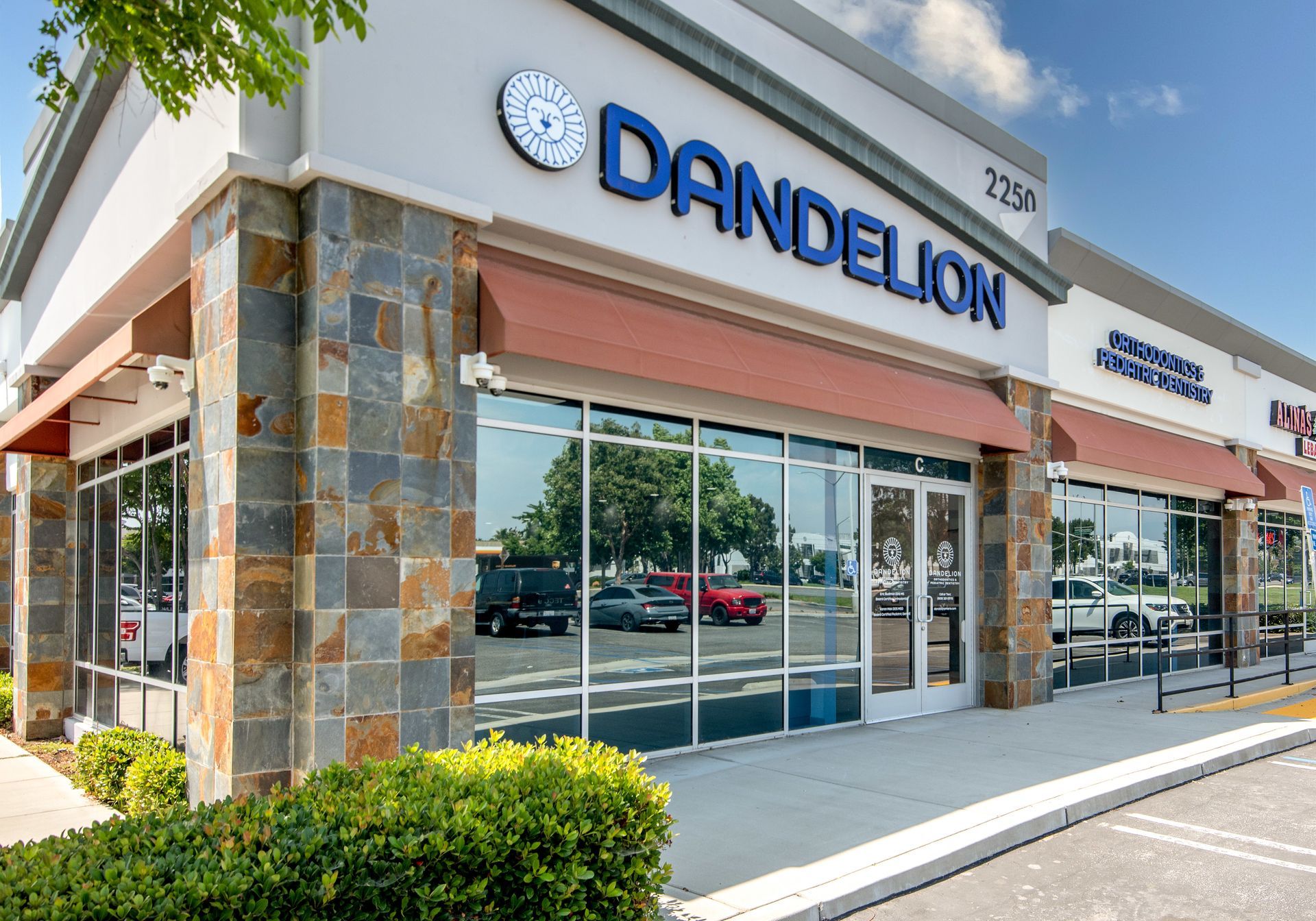 Dandelion storefront with blue sign, tan awning, stone accents, and reflective windows; outdoors.