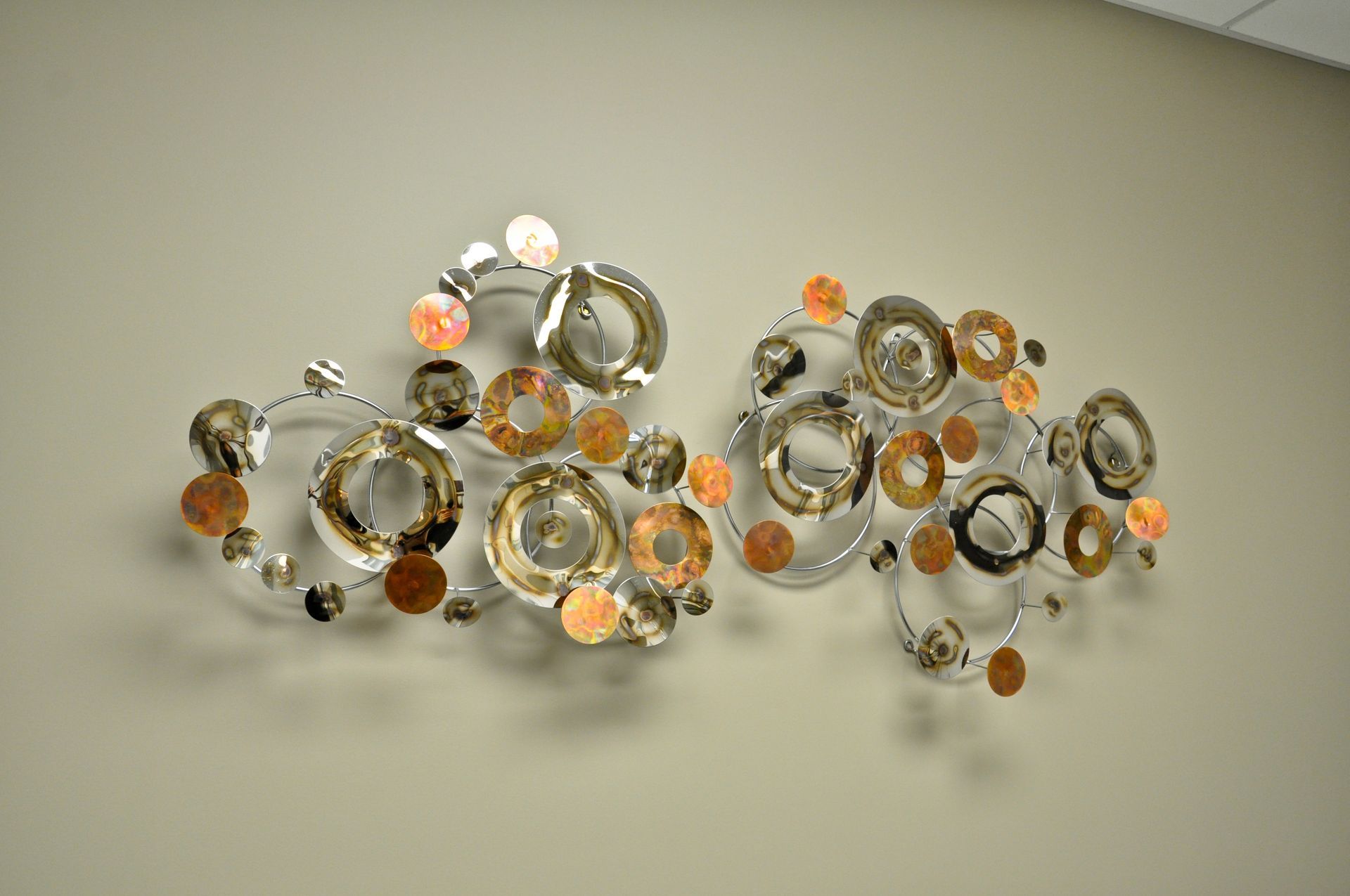 Wall art: metallic sculpture with overlapping circles and copper accents on a beige wall.