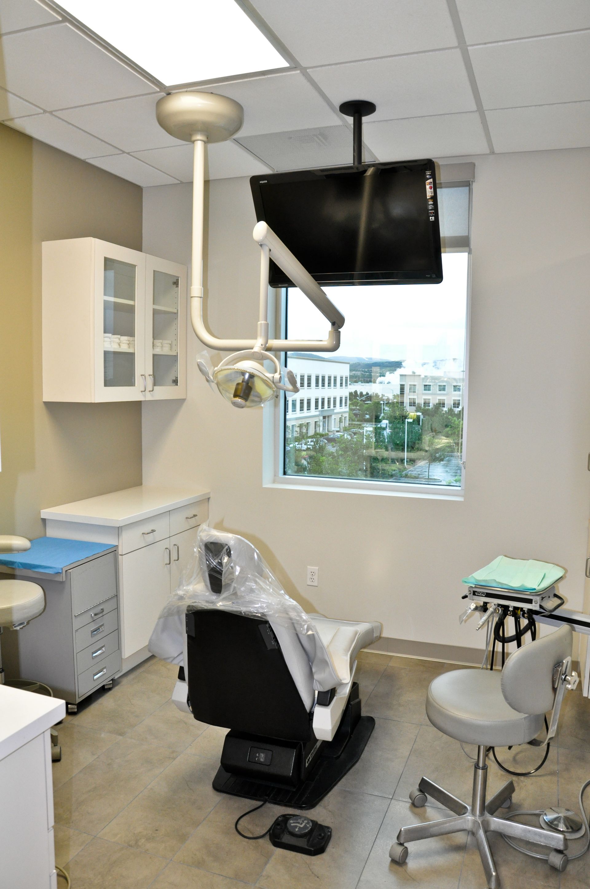 Dental exam room with chair, light, cabinets, and window with a view.
