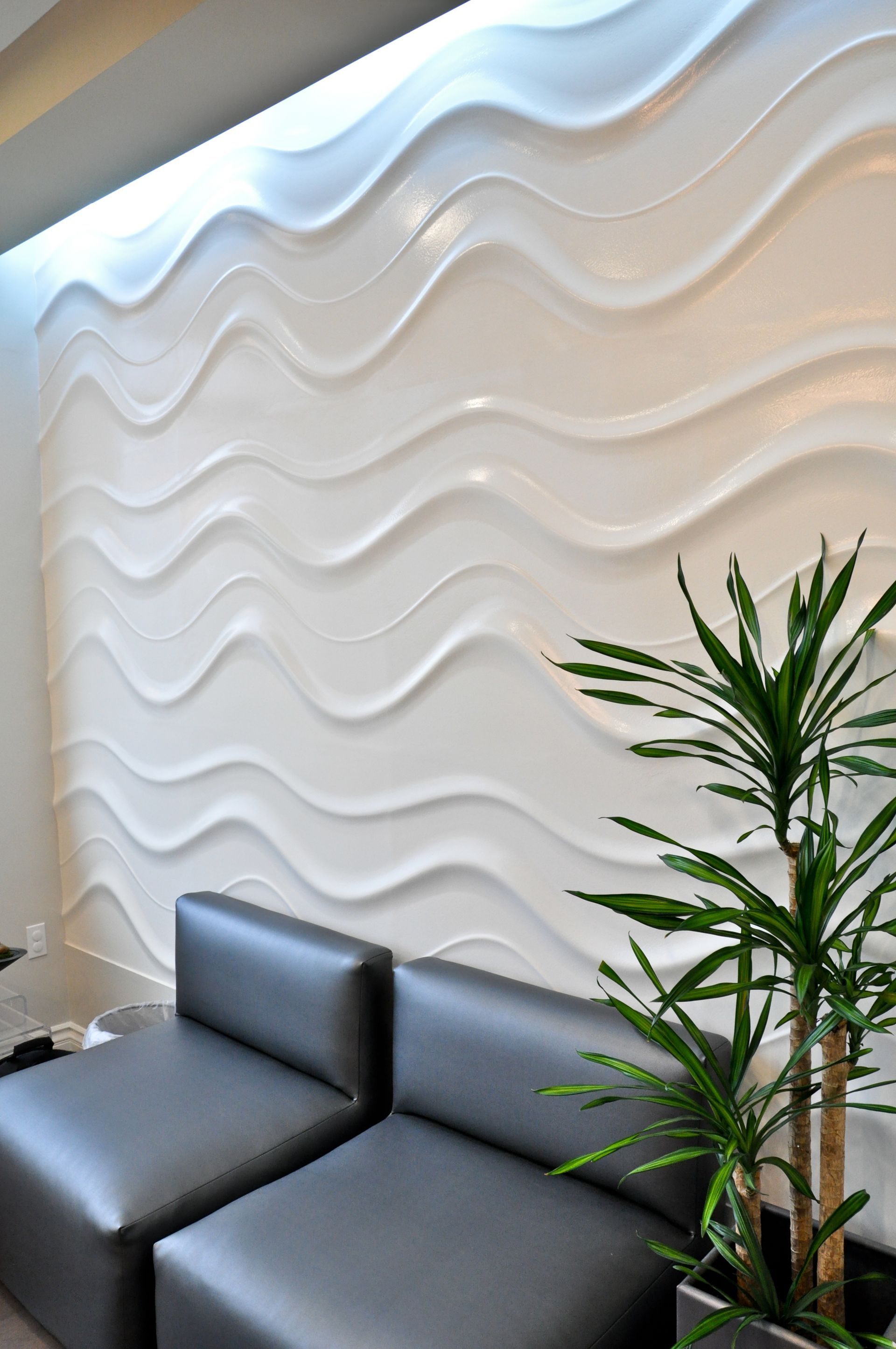 White wavy textured wall with a black couch and green plant.